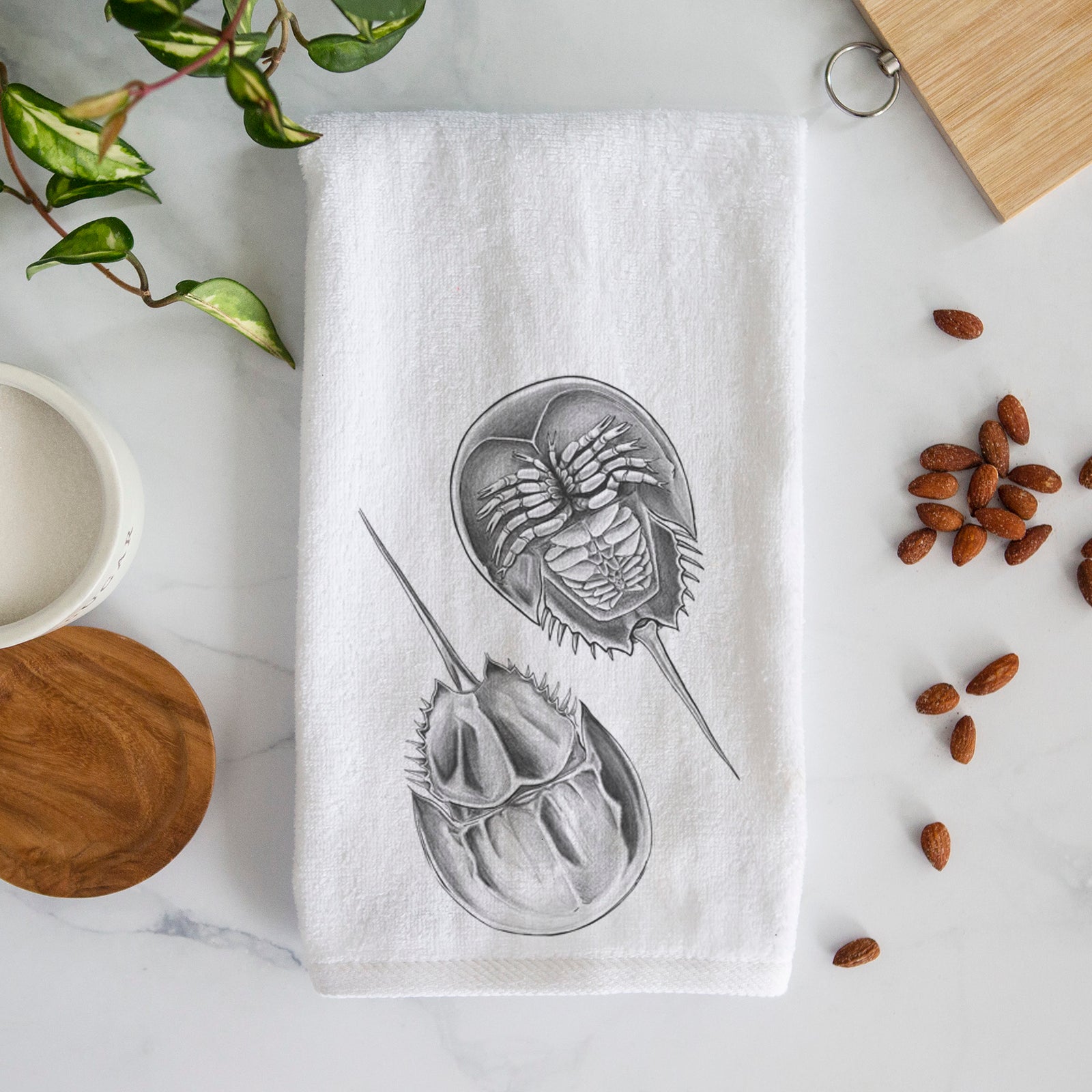White hand towel printed with a detailed black ink illustration of two horseshoe crabs.