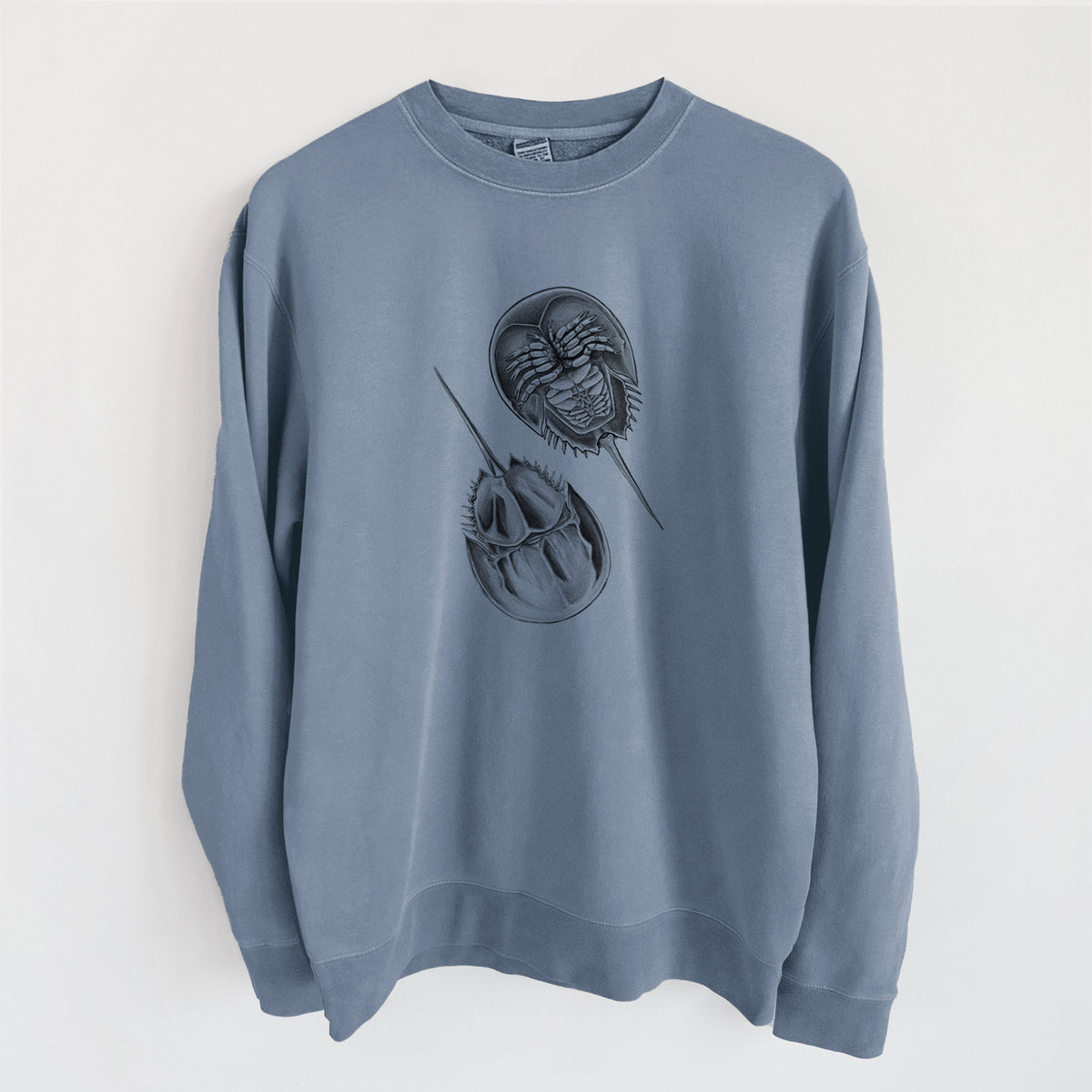 Slate blue pigment dyed crewneck sweatshirt laid flat, printed with a detailed black ink illustration of two horseshoe crabs.