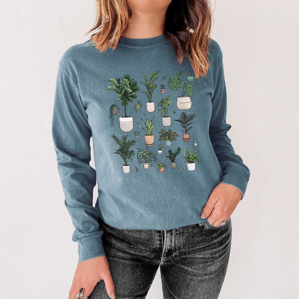 Steel blue Comfort Colors long sleeve shirt printed with a full-color collection of potted houseplants in different pots, shown in a lifestyle photo.