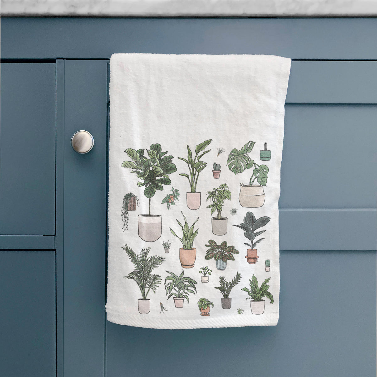 White hand towel printed with a full-color collection of potted houseplants in different pots, hanging on a cabinet door.