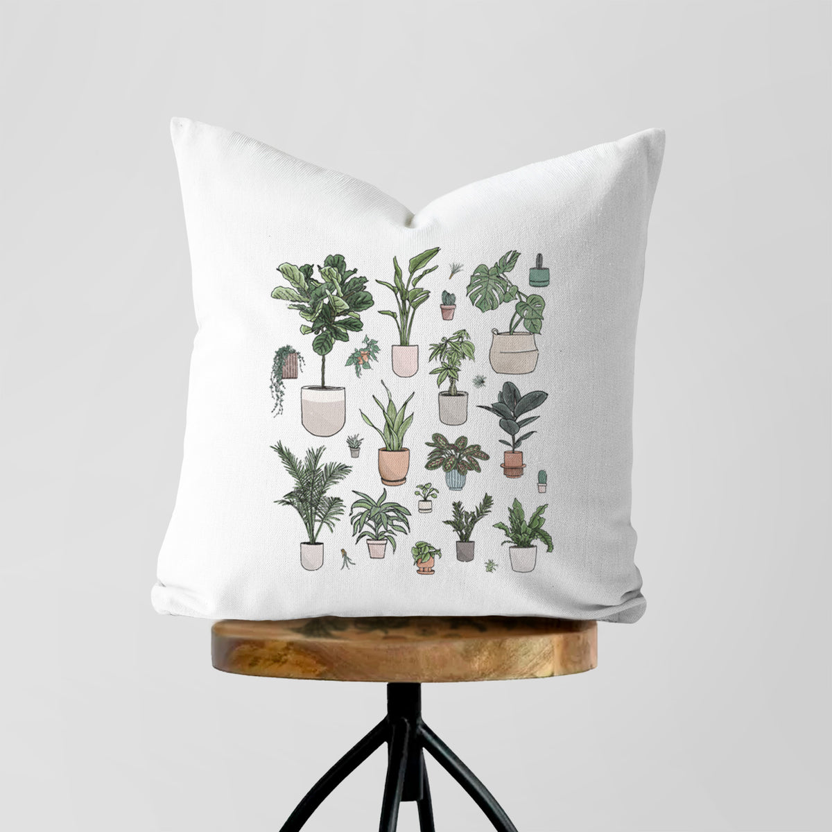 White pillow cover printed with a full-color collection of potted houseplants in different pots, on a wooden stool.