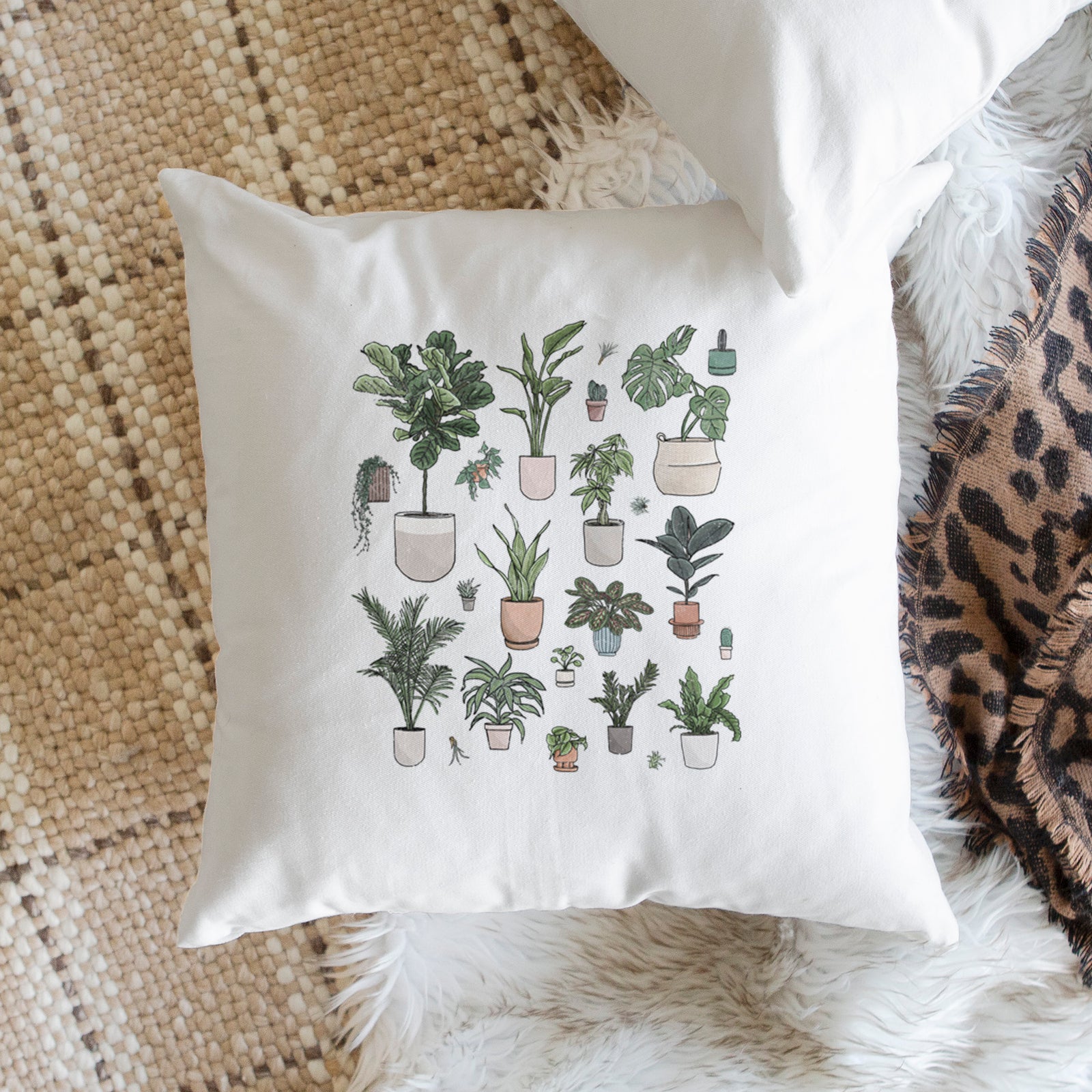White pillow cover printed with a full-color collection of potted houseplants in different pots, on a bench beside plants.