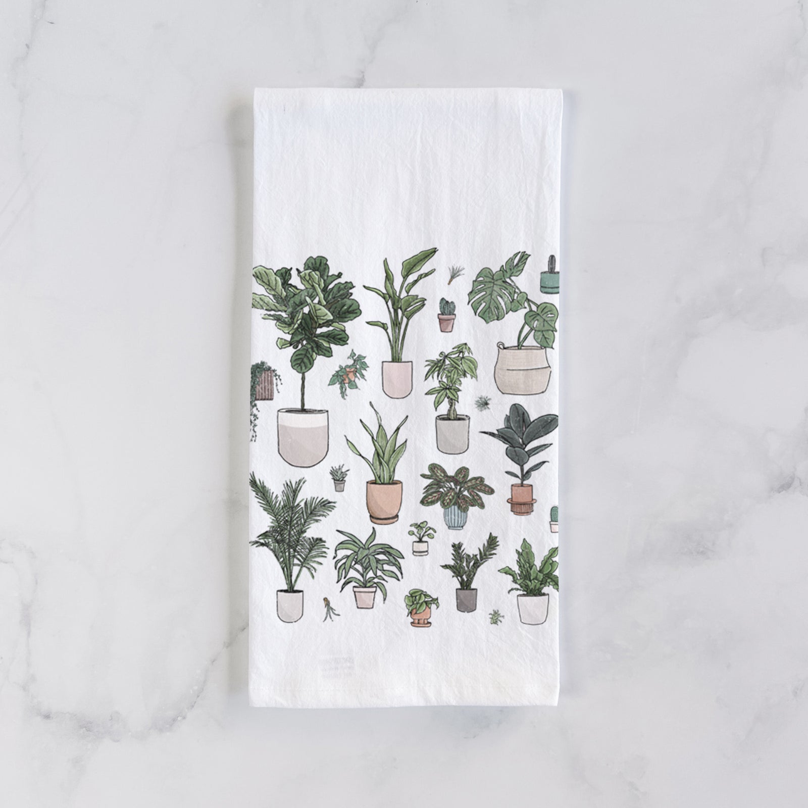 White cotton tea towel printed with a full-color collection of potted houseplants in different pots, on a marble counter beside a round wooden cutting board and greenery.