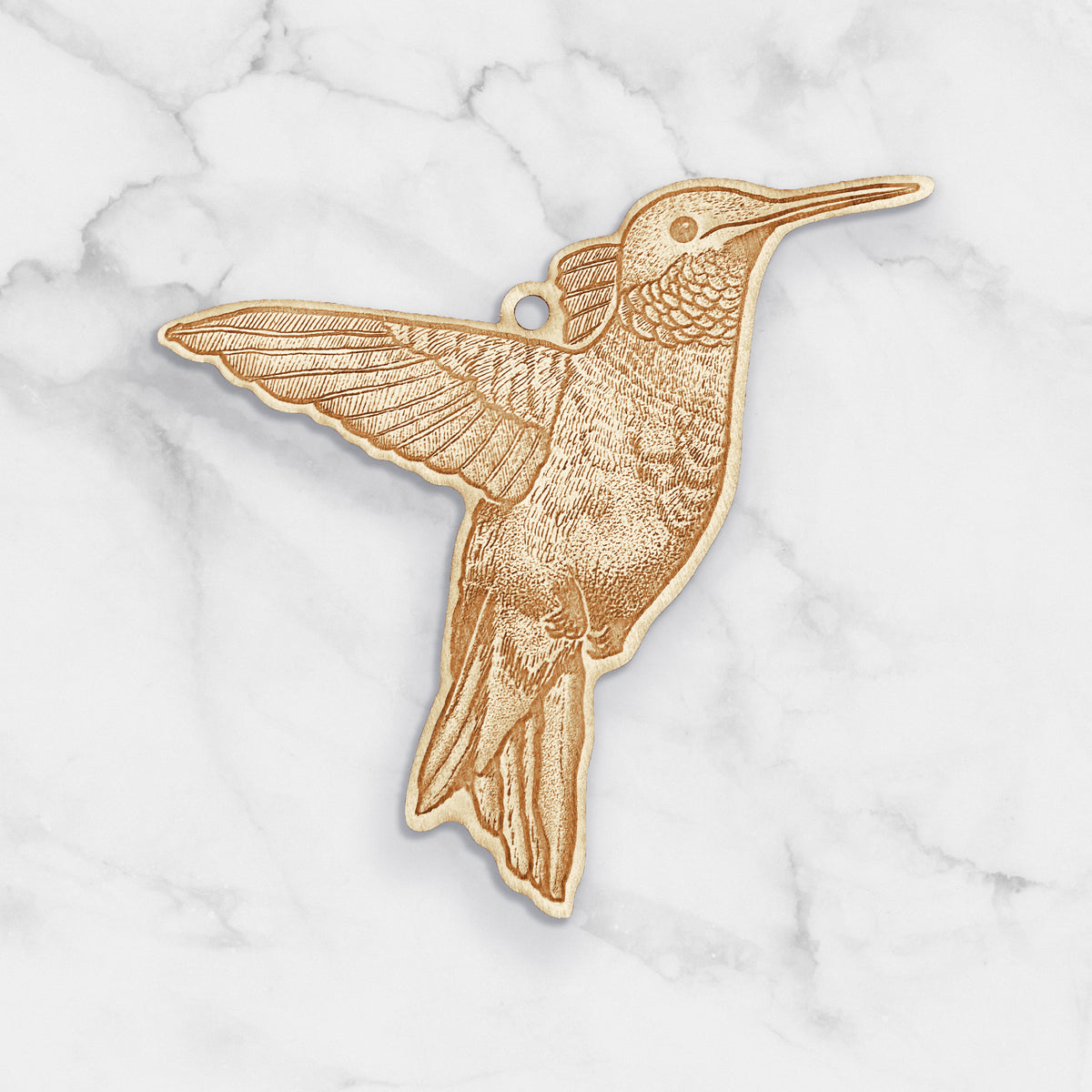Wooden ornament featuring a detailed engraving of a hummingbird in flight, on a marble surface.