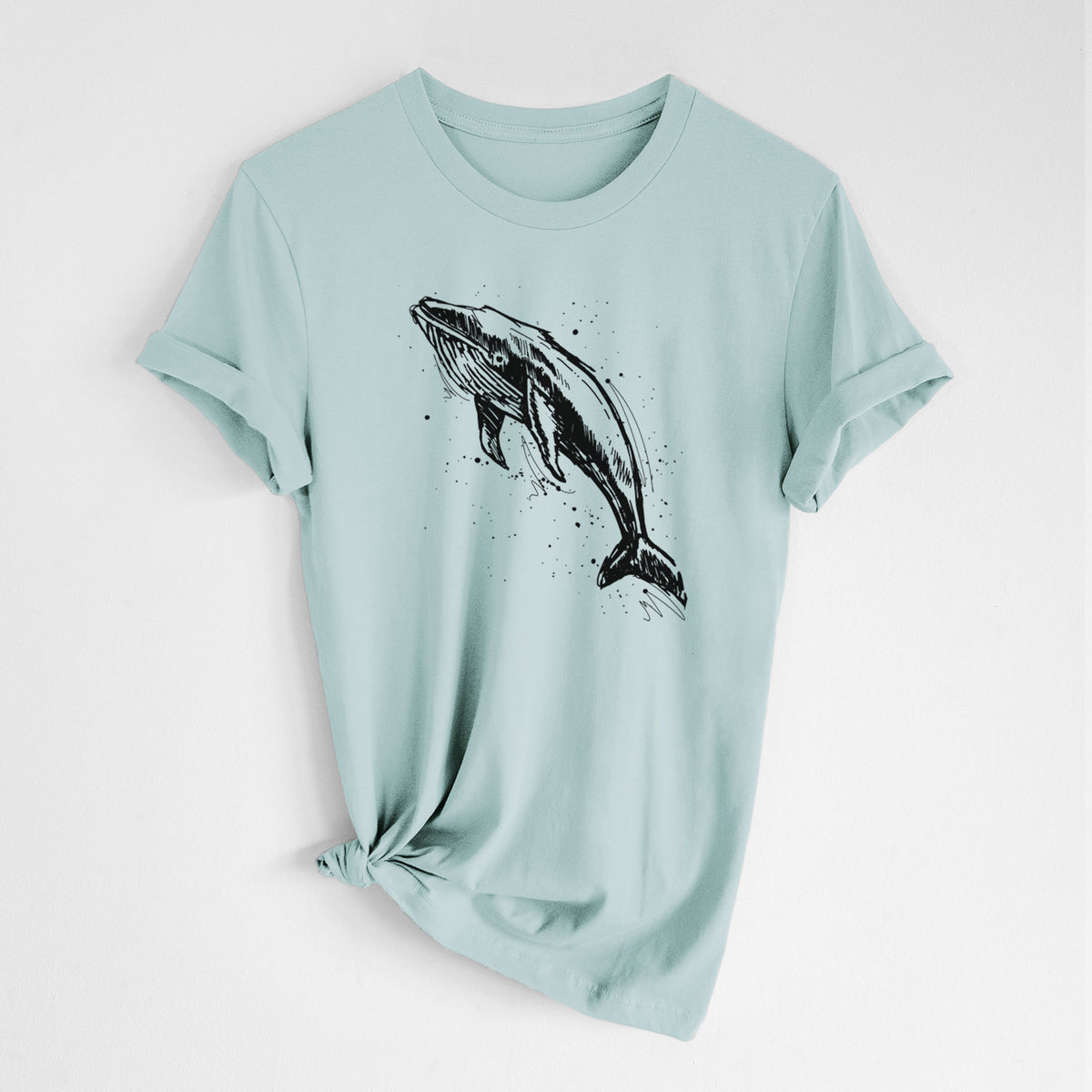 Dusty blue lightweight cotton t-shirt laid flat with the sleeves rolled, printed with a black ink illustration of a humpback whale diving, with ink splatters.