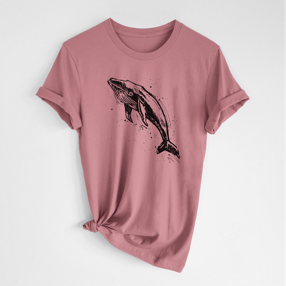 Mauve pink lightweight cotton t-shirt laid flat with the sleeves rolled, printed with a black ink illustration of a humpback whale diving, with ink splatters.