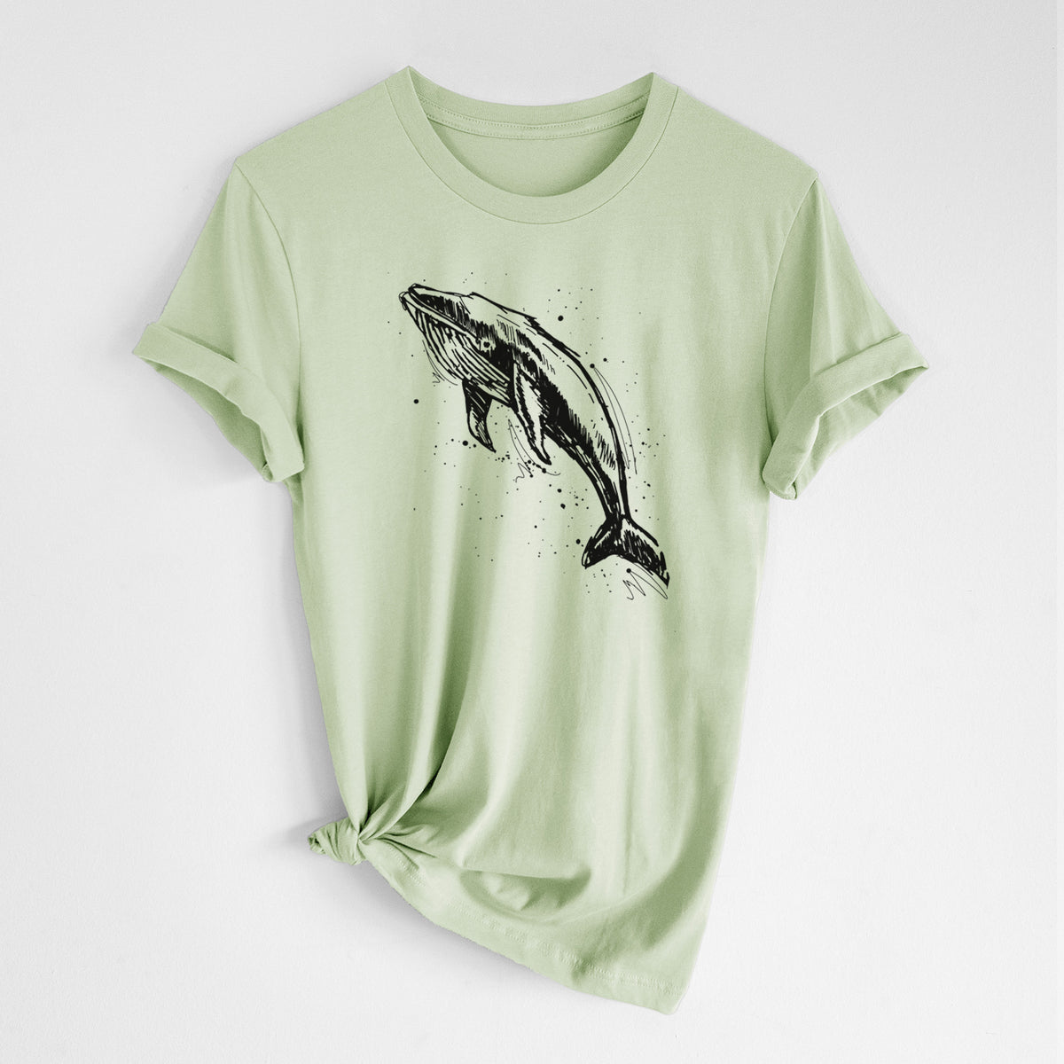 Spring green lightweight cotton t-shirt laid flat with the sleeves rolled, printed with a black ink illustration of a humpback whale diving, with ink splatters.