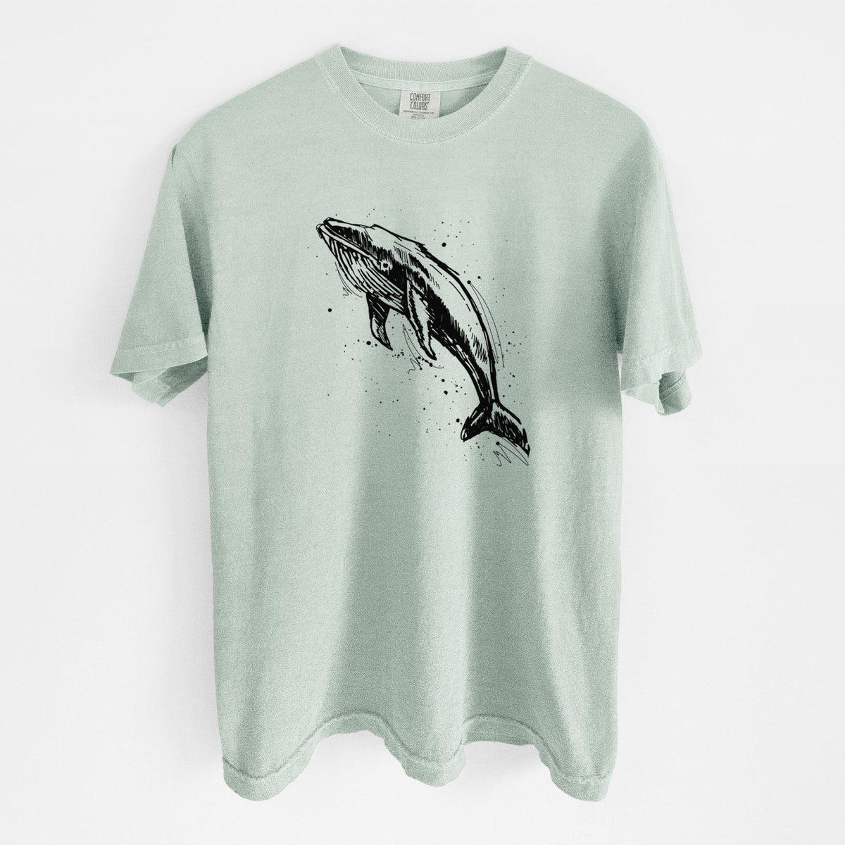 Bay green Comfort Colors t-shirt laid flat, printed with a black ink illustration of a humpback whale diving, with ink splatters.