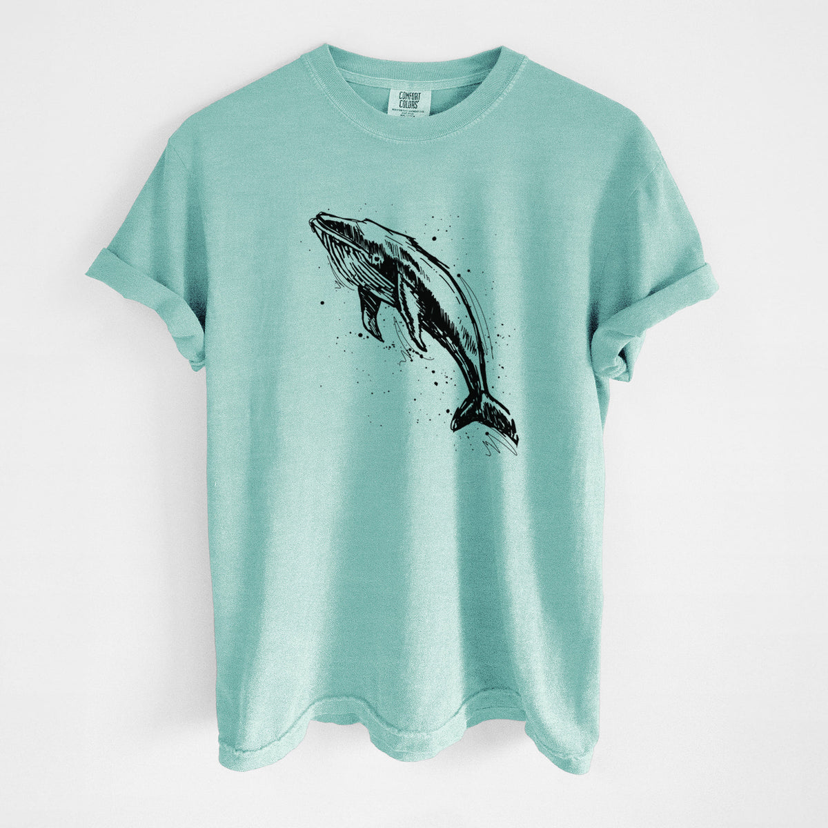 Chalky mint Comfort Colors t-shirt laid flat, printed with a black ink illustration of a humpback whale diving, with ink splatters.