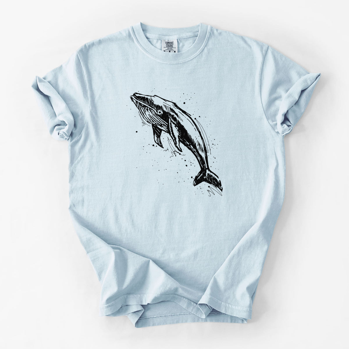 Chambray blue Comfort Colors t-shirt laid flat, printed with a black ink illustration of a humpback whale diving, with ink splatters.