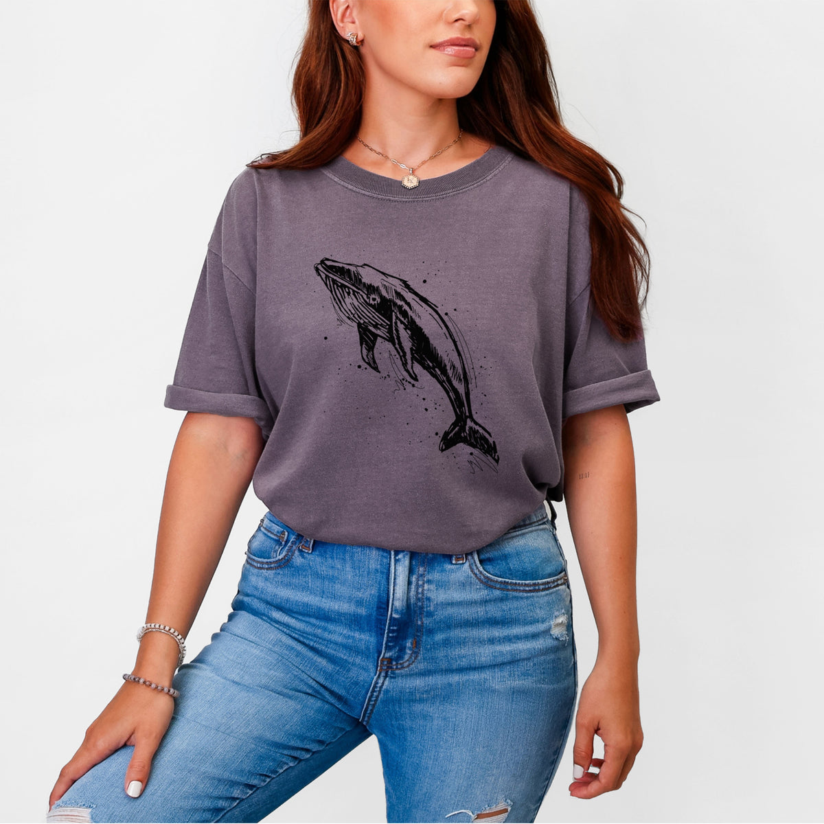 Woman wearing a Comfort Colors t-shirt printed with a black ink illustration of a humpback whale diving, with ink splatters.