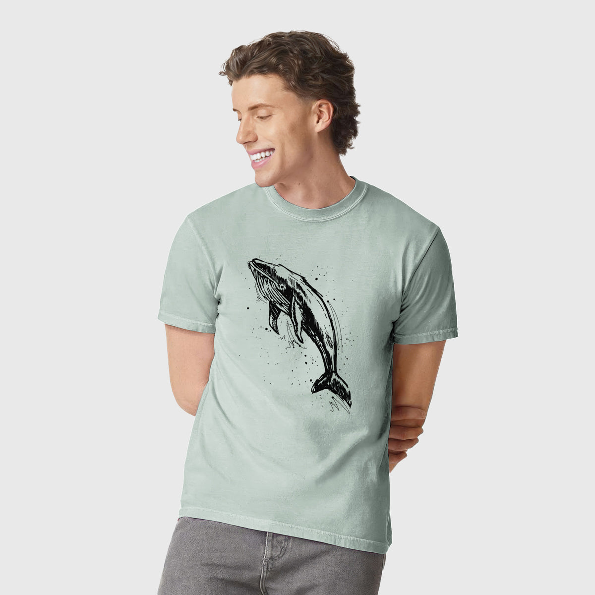 Man wearing a Comfort Colors t-shirt printed with a black ink illustration of a humpback whale diving, with ink splatters.