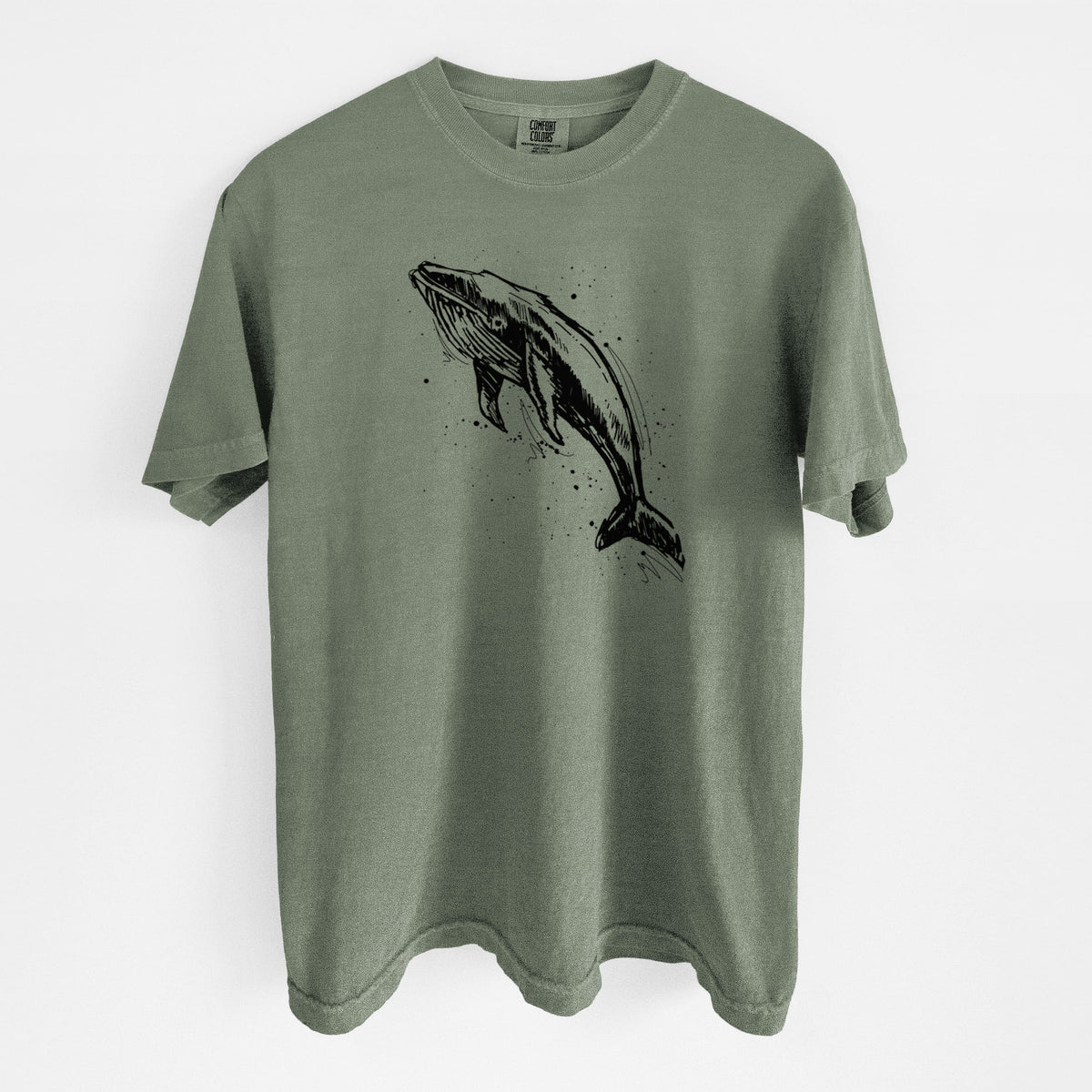 Moss green Comfort Colors t-shirt laid flat, printed with a black ink illustration of a humpback whale diving, with ink splatters.