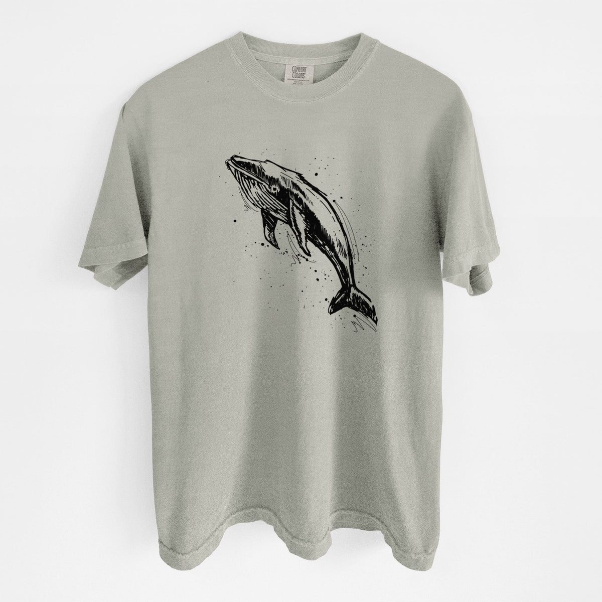 Sandstone beige Comfort Colors t-shirt laid flat, printed with a black ink illustration of a humpback whale diving, with ink splatters.