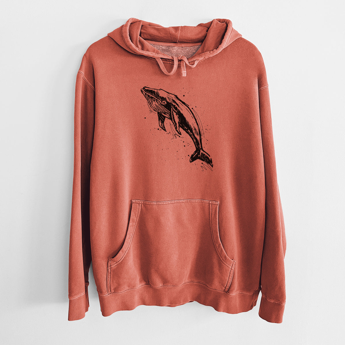 Amber orange pigment dyed hoodie laid flat, printed with a black ink illustration of a humpback whale diving, with ink splatters.