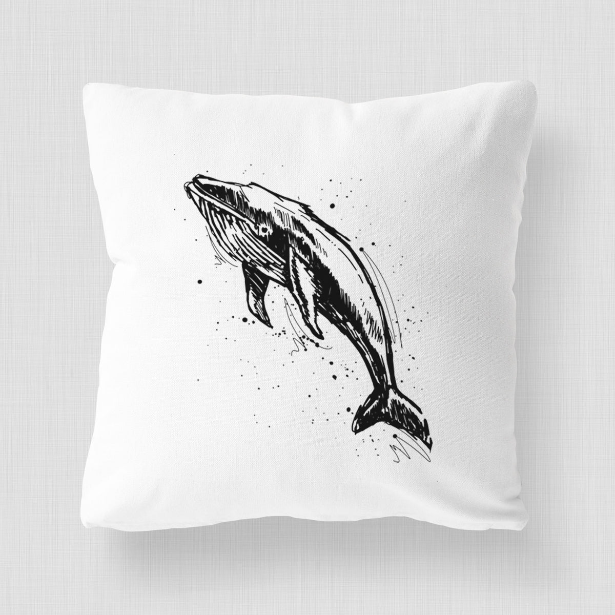 White pillow cover printed with a black ink illustration of a humpback whale diving, with ink splatters.