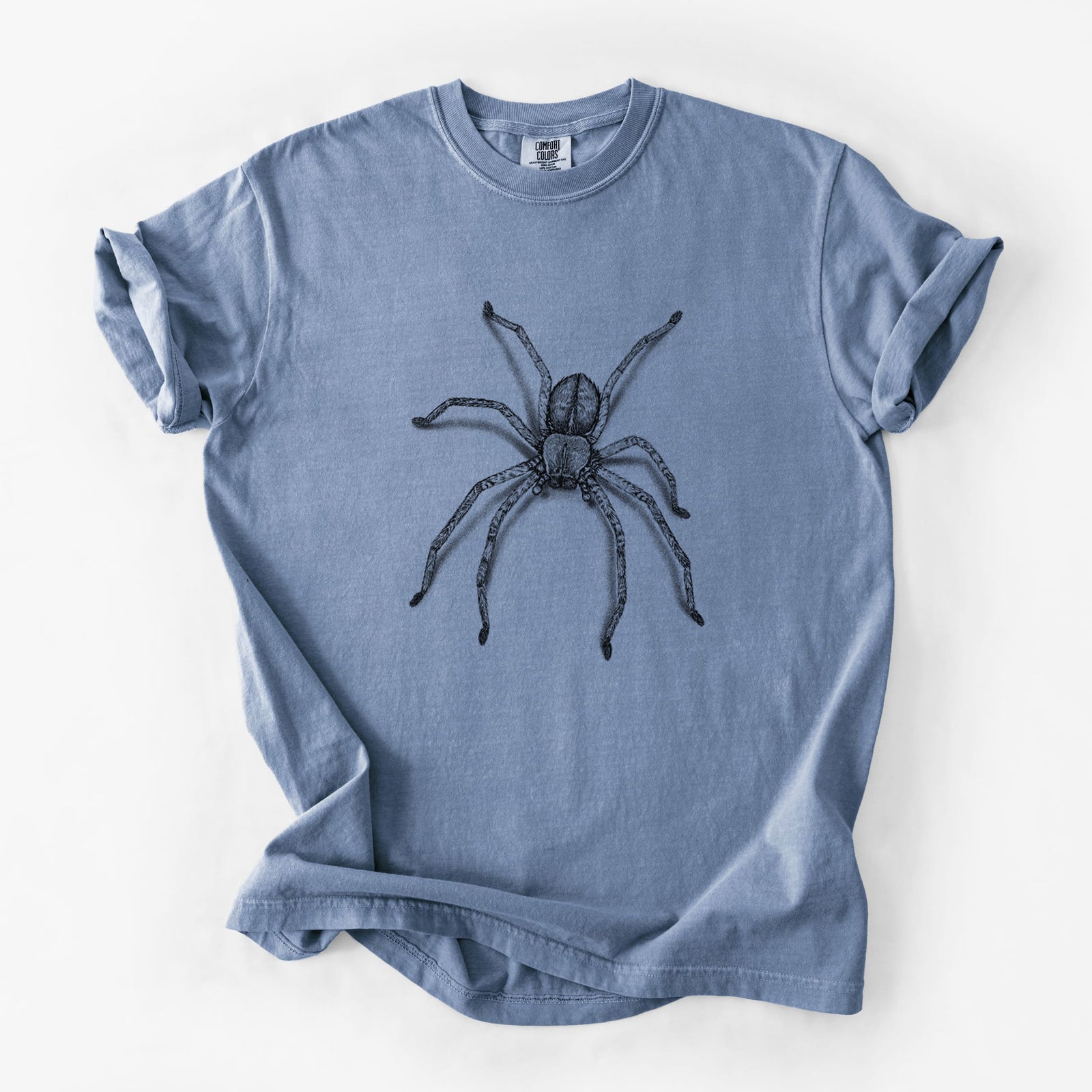 Blue jean Comfort Colors t-shirt laid flat, printed with a detailed black ink illustration of a huntsman spider with long legs spread.