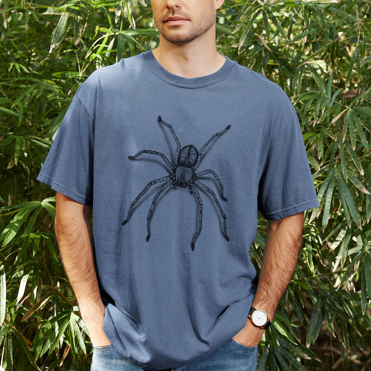 Man wearing a Comfort Colors t-shirt printed with a detailed black ink illustration of a huntsman spider with long legs spread, outdoors.
