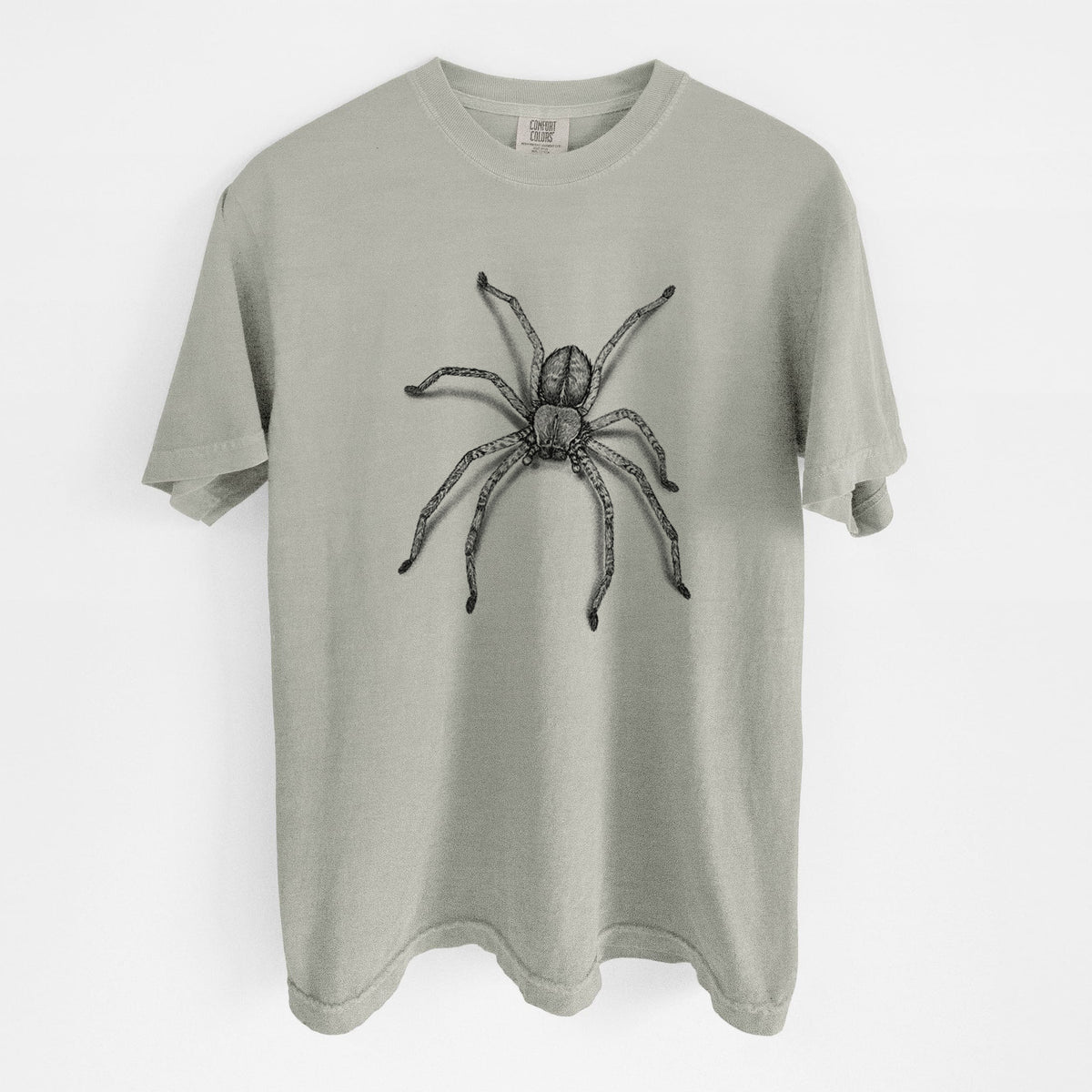 Sandstone beige Comfort Colors t-shirt laid flat, printed with a detailed black ink illustration of a huntsman spider with long legs spread.