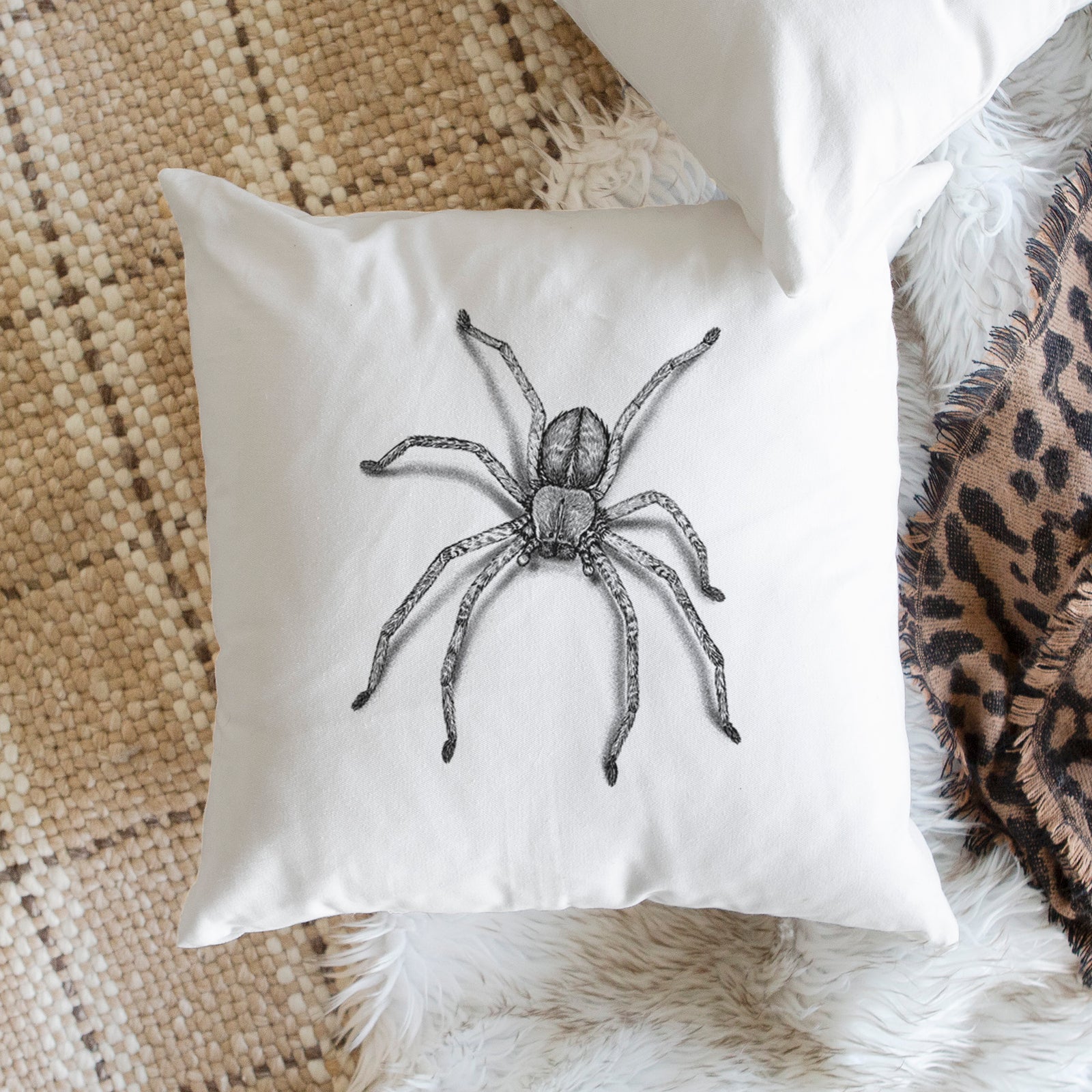 White pillow cover printed with a detailed black ink illustration of a huntsman spider with long legs spread, on a bench beside plants.