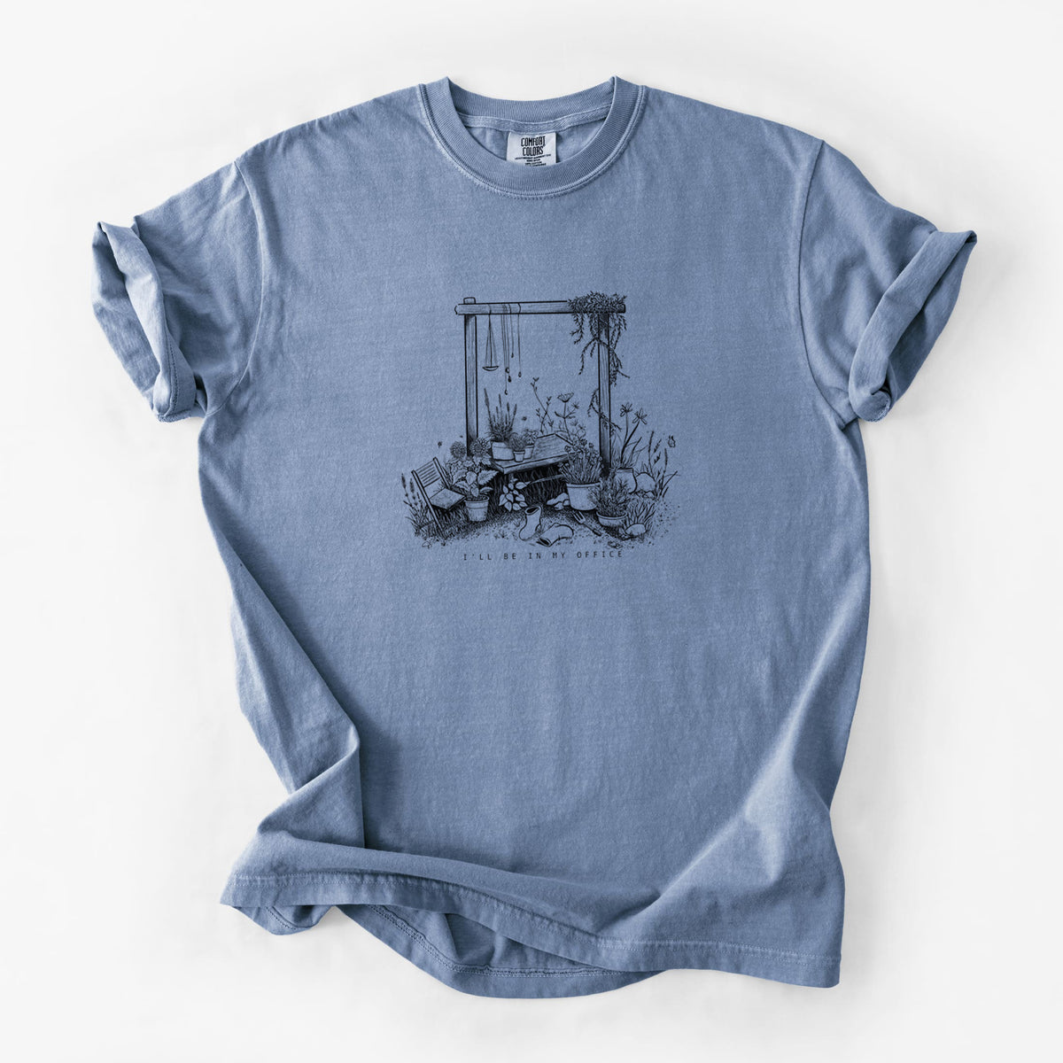 Blue jean Comfort Colors t-shirt laid flat, printed with a black ink illustration of a garden gate arch surrounded by potted plants and flowers.