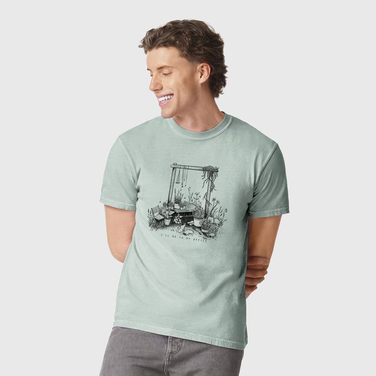 Man wearing a Comfort Colors t-shirt printed with a black ink illustration of a garden gate arch surrounded by potted plants and flowers.