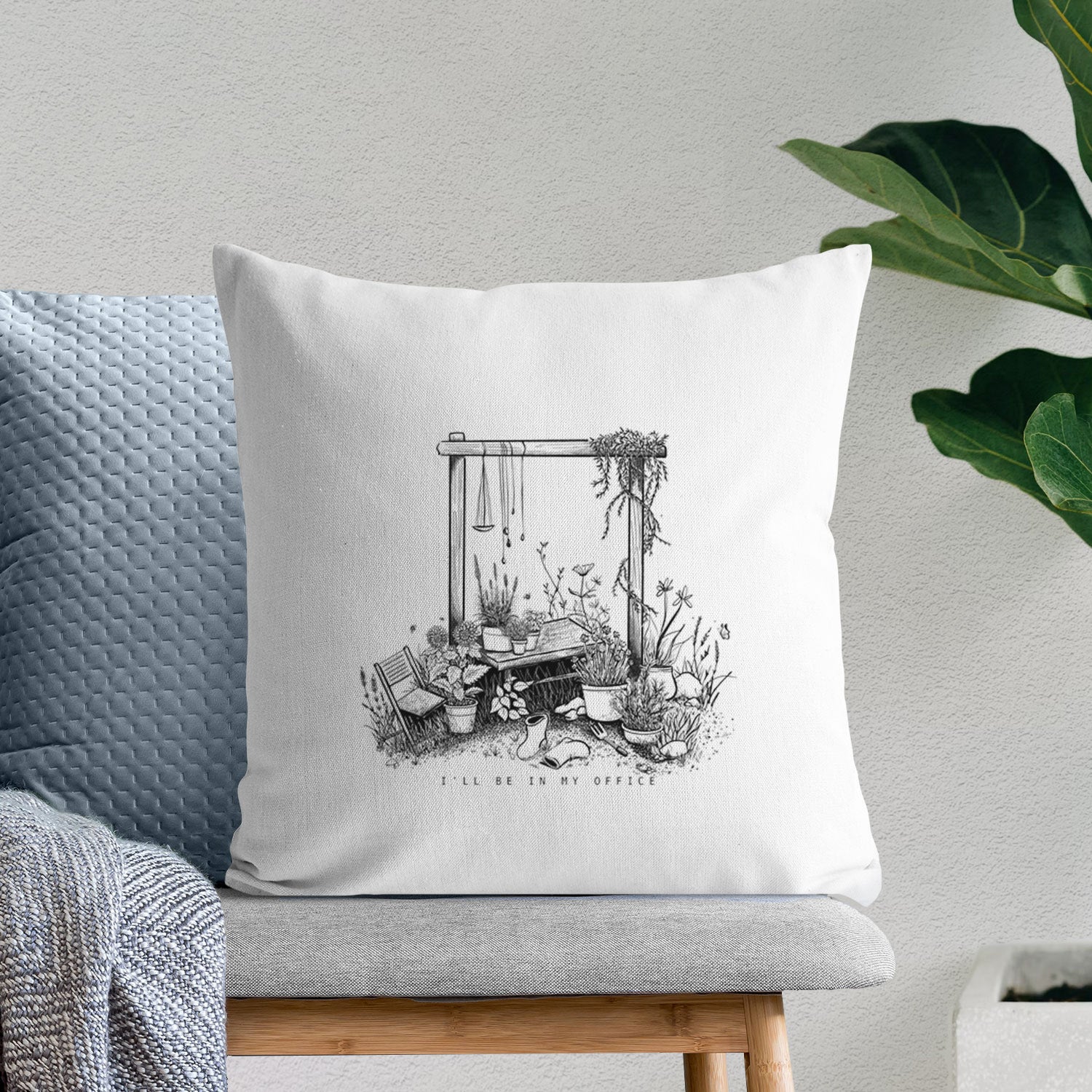 White pillow cover printed with a black ink illustration of a garden gate arch surrounded by potted plants and flowers, on a bench beside plants.