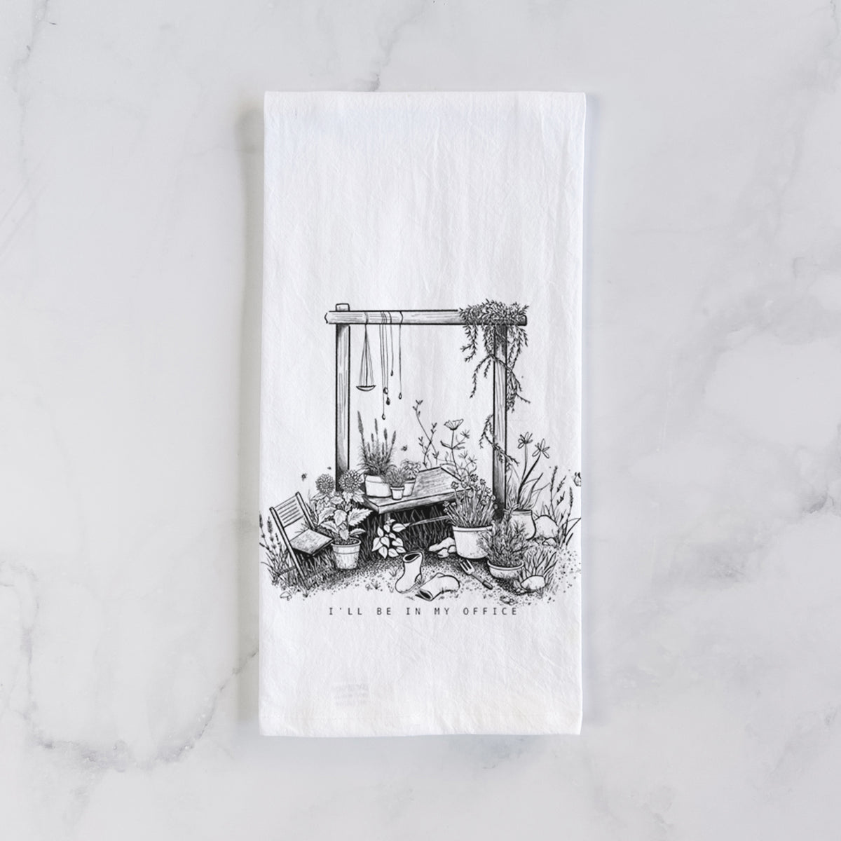 White cotton tea towel laid flat on marble, printed with a black ink illustration of a garden gate arch surrounded by potted plants and flowers.