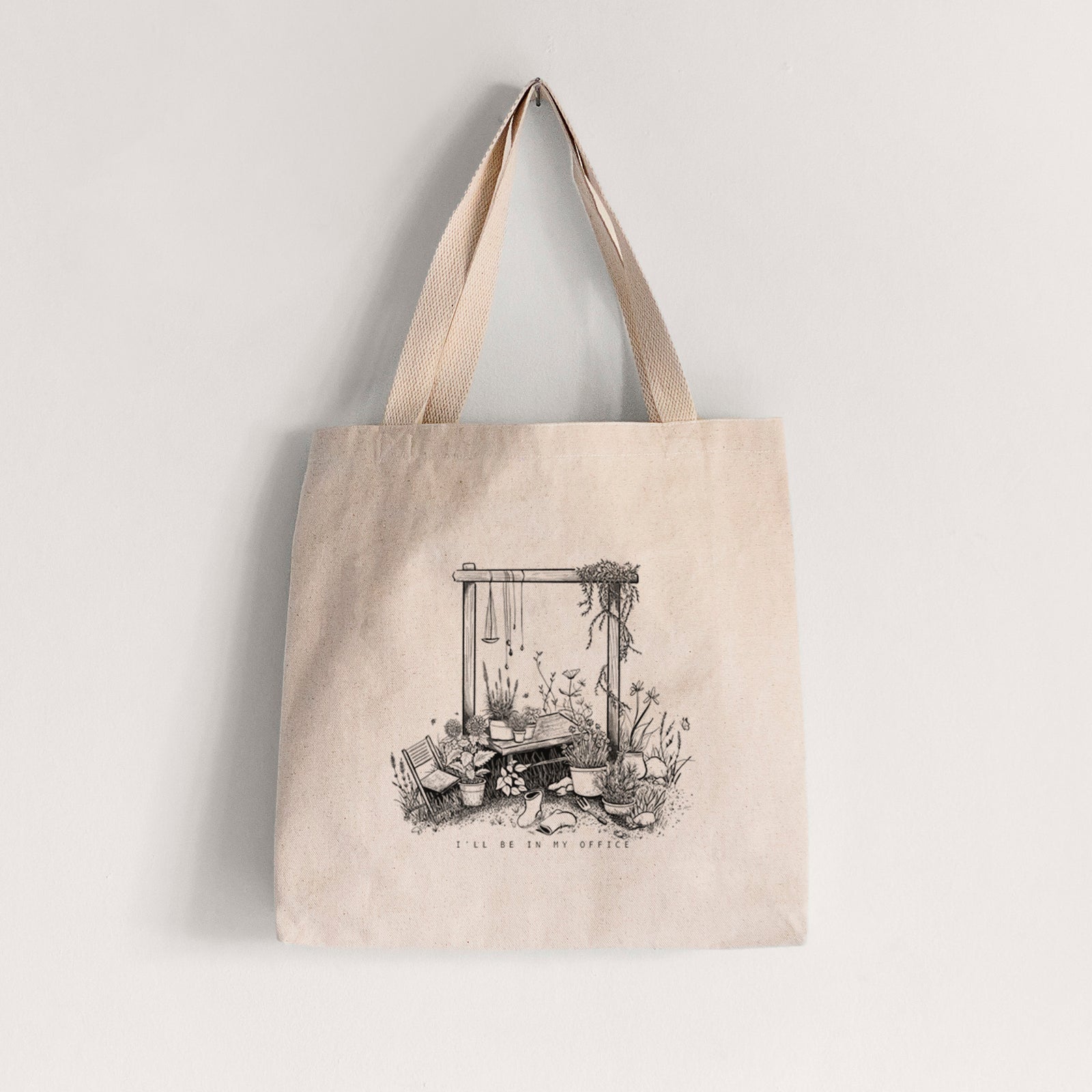 Natural canvas tote bag printed with a black ink illustration of a garden gate arch surrounded by potted plants and flowers.