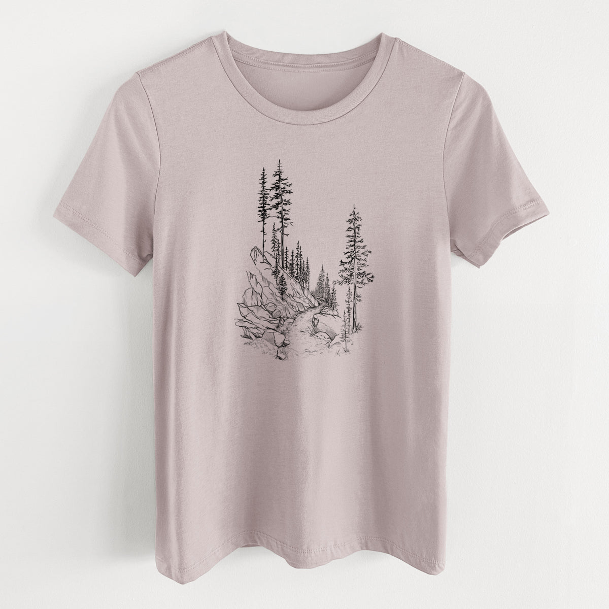 Pink gravel women's relaxed fit cotton t-shirt laid flat, printed with a black ink illustration of a trail winding past tall pine trees and rocks into the woods.