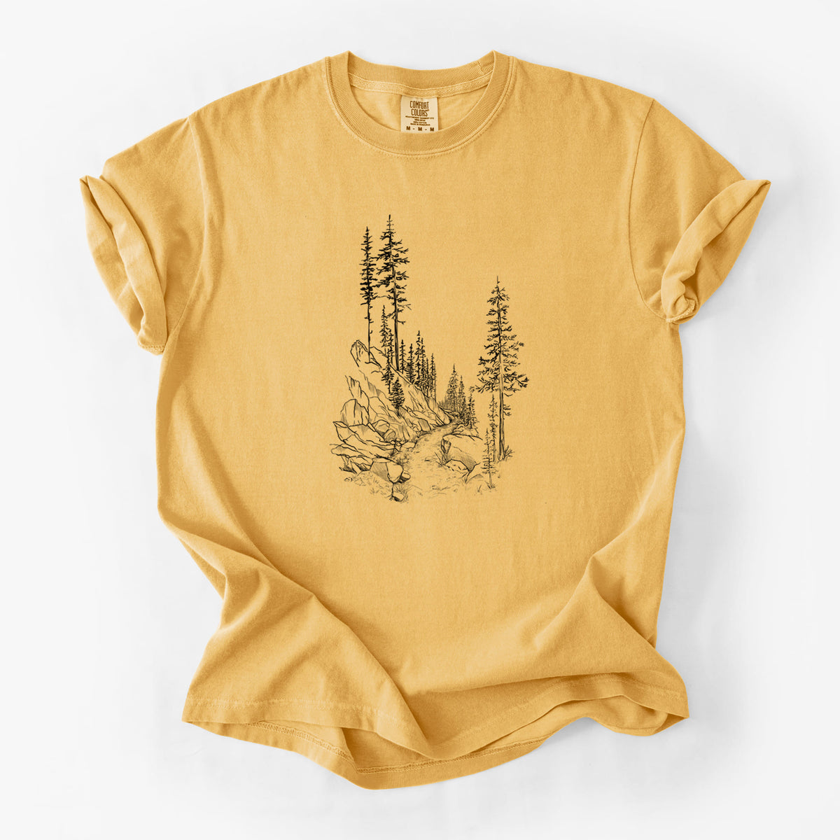 Golden wheat yellow Comfort Colors t-shirt laid flat, printed with a black ink illustration of a trail winding past tall pine trees and rocks into the woods.