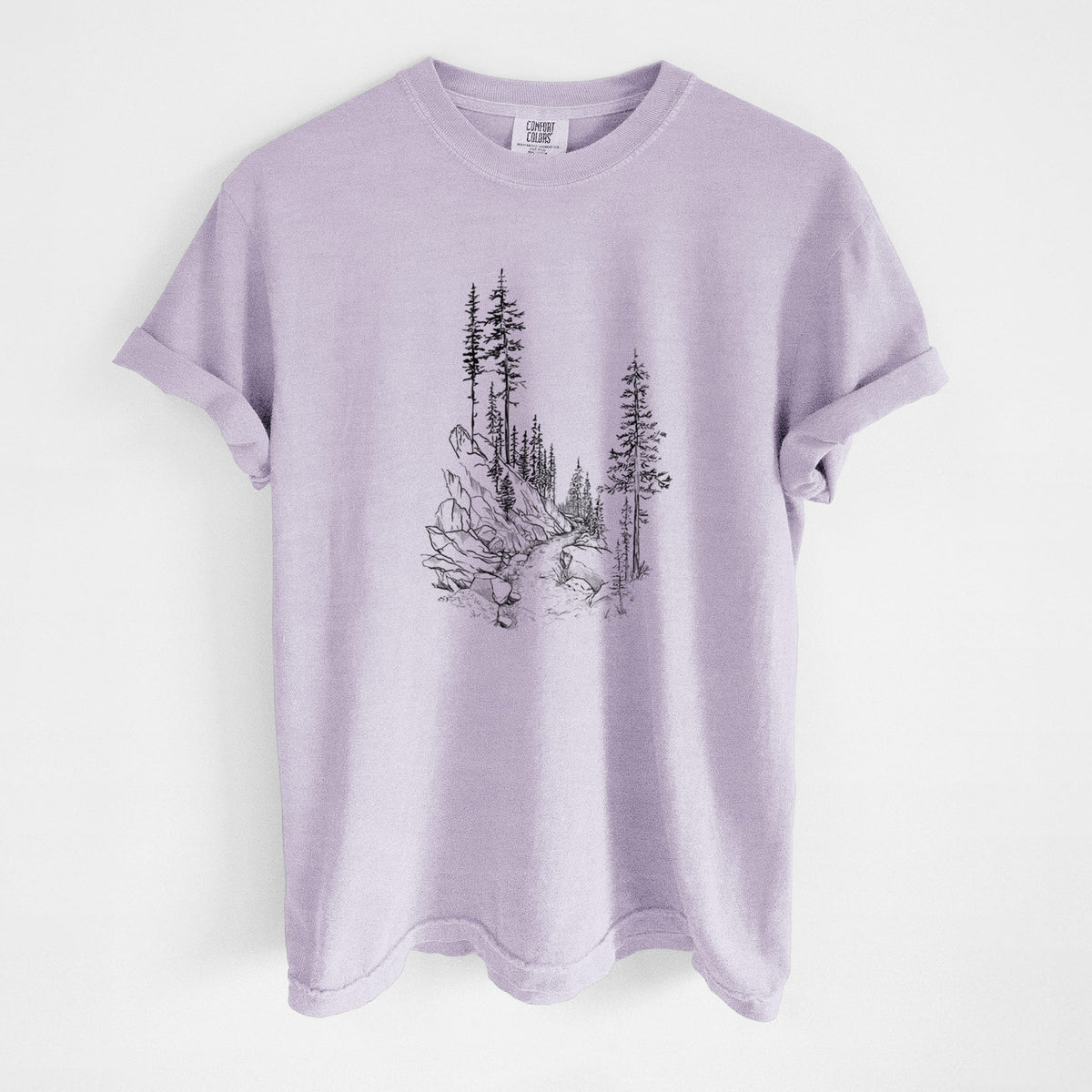 Orchid purple Comfort Colors t-shirt laid flat, printed with a black ink illustration of a trail winding past tall pine trees and rocks into the woods.