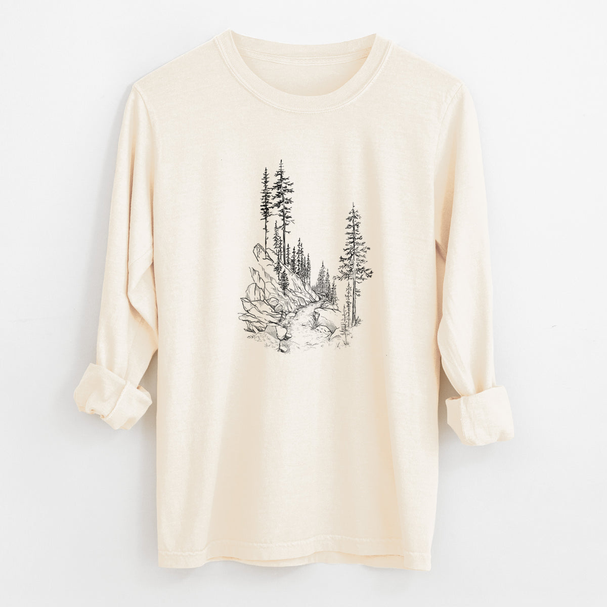Ivory Comfort Colors long sleeve shirt laid flat with the cuffs rolled, printed with a black ink illustration of a trail winding past tall pine trees and rocks into the woods.