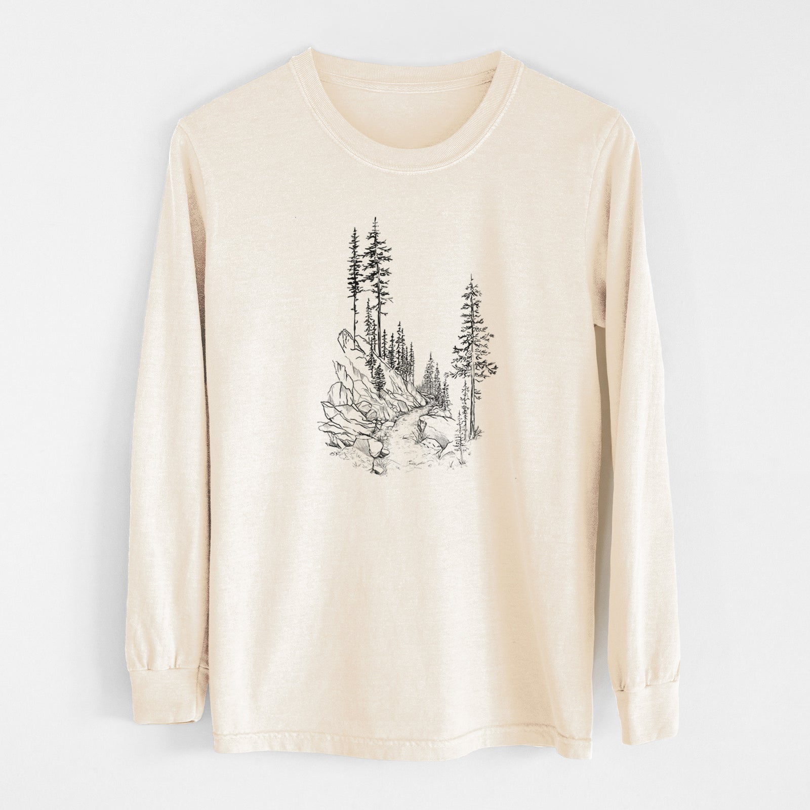 Ivory Comfort Colors long sleeve shirt laid flat, printed with a black ink illustration of a trail winding past tall pine trees and rocks into the woods.