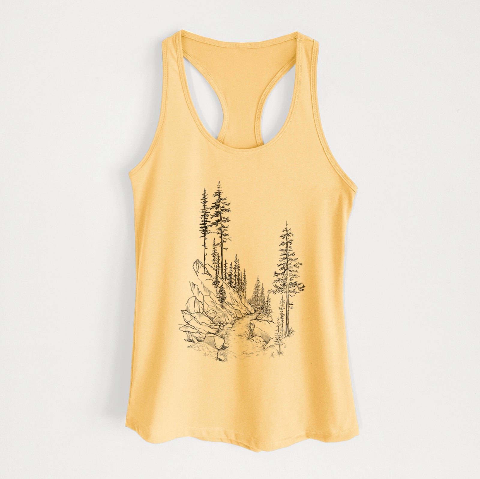 Banana cream women's racerback tank top laid flat, printed with a black ink illustration of a trail winding past tall pine trees and rocks into the woods.