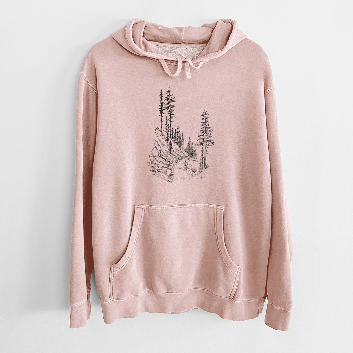 Dusty pink pigment dyed hoodie laid flat, printed with a black ink illustration of a trail winding past tall pine trees and rocks into the woods.