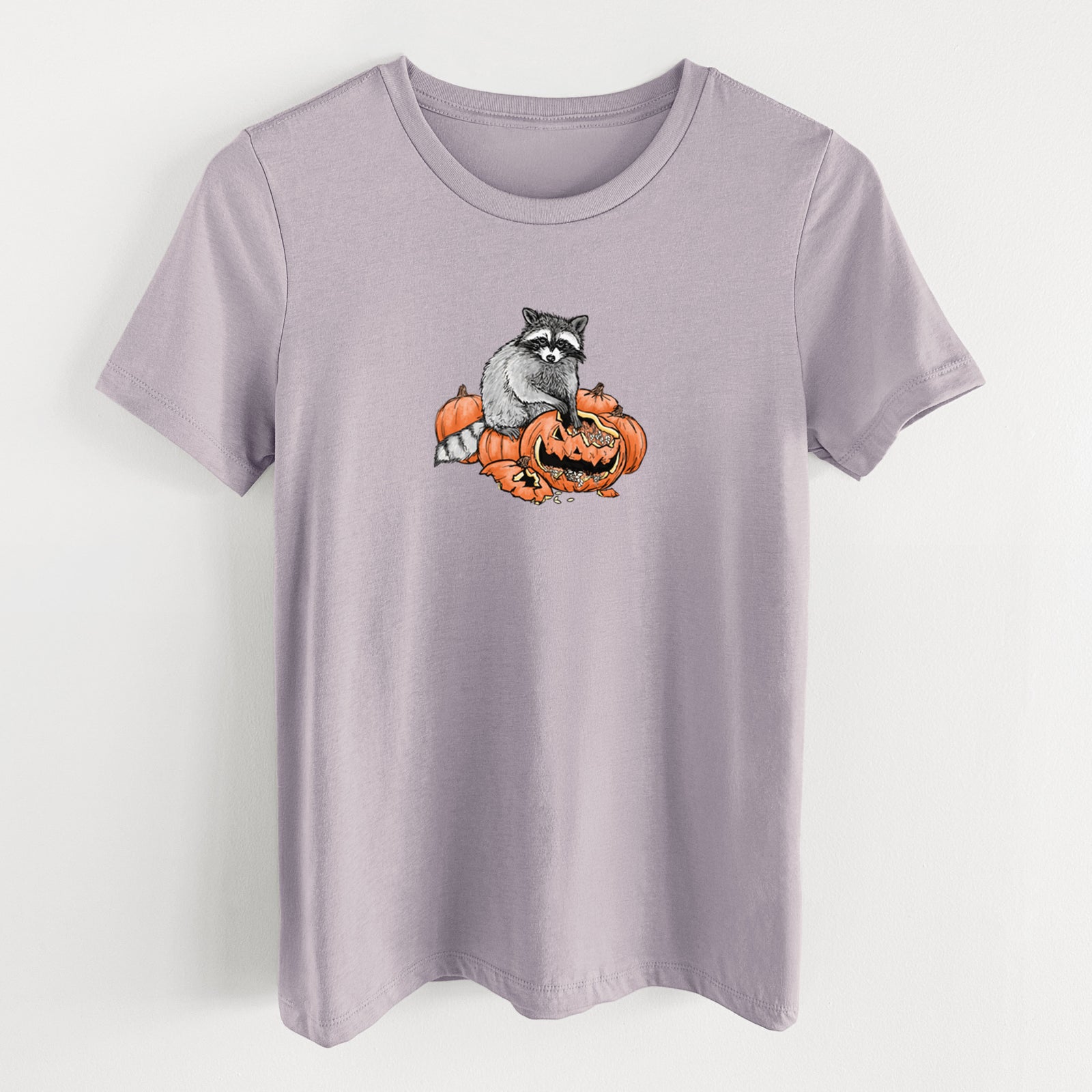 Light violet women's relaxed fit cotton t-shirt laid flat, printed with a black ink raccoon peeking over carved orange jack-o'-lanterns.