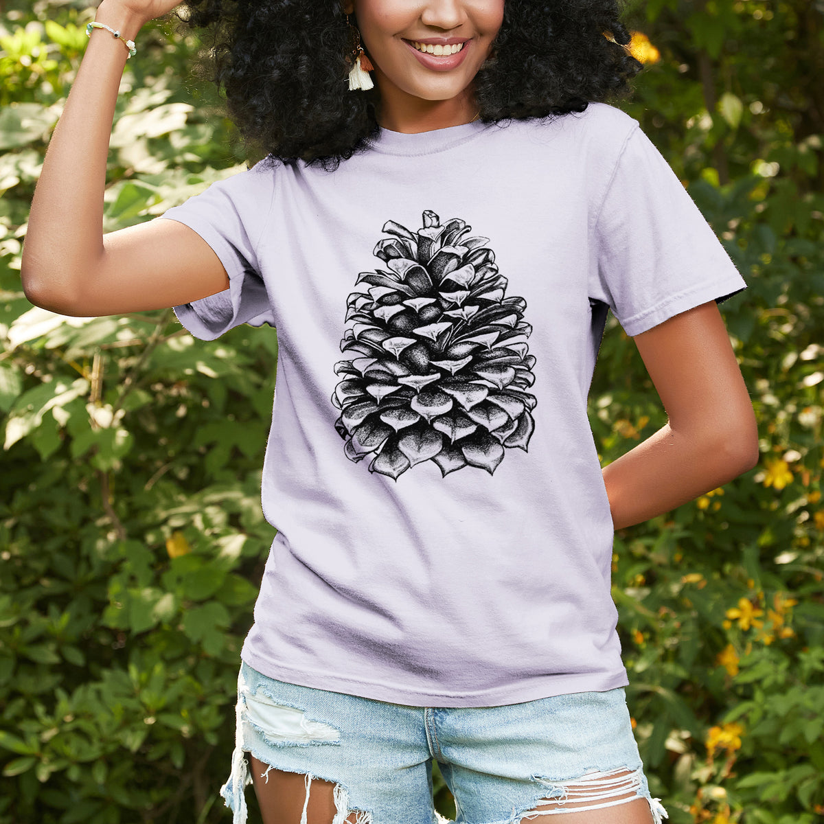 Woman wearing a Comfort Colors t-shirt printed with a detailed black ink illustration of a large Jeffrey pine cone, outdoors.