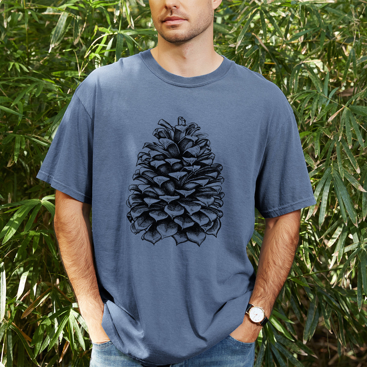 Man wearing a Comfort Colors t-shirt printed with a detailed black ink illustration of a large Jeffrey pine cone, outdoors.
