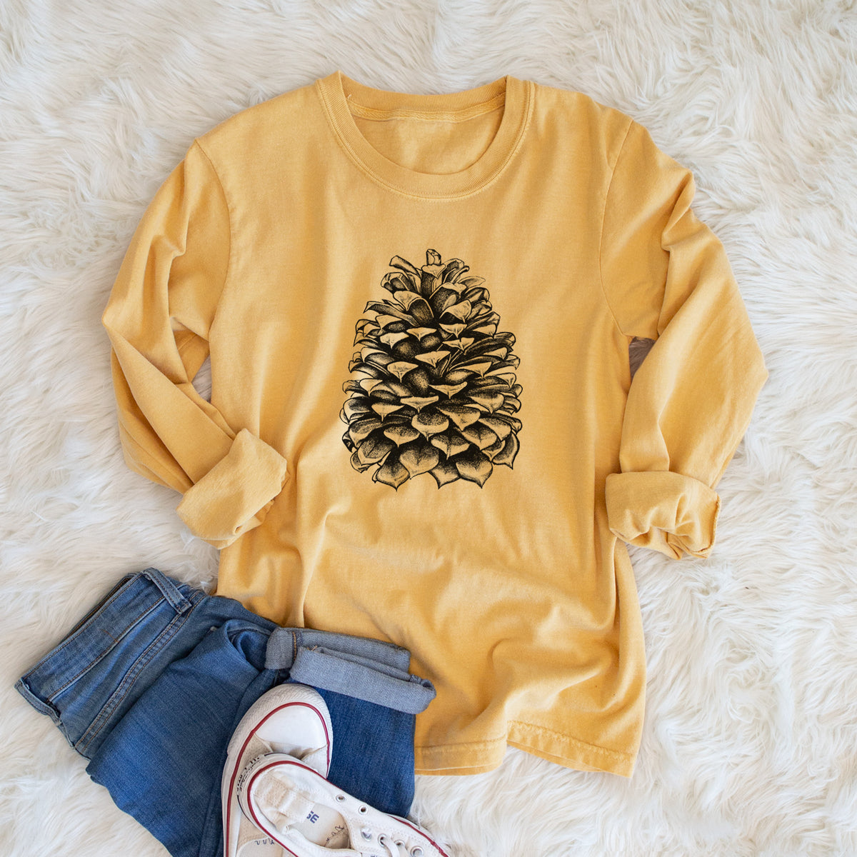 Golden wheat yellow Comfort Colors long sleeve shirt printed with a detailed black ink illustration of a large Jeffrey pine cone, shown in a lifestyle photo.