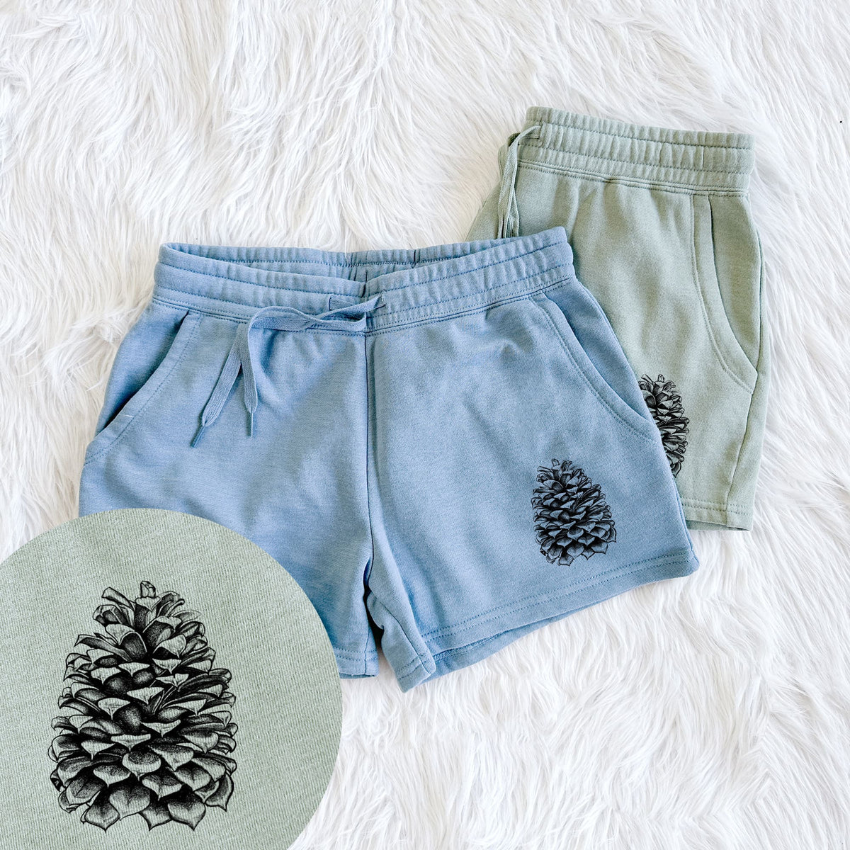 Two pairs of Cali Wave shorts in different colors printed with a detailed black ink illustration of a large Jeffrey pine cone, with a close-up of the print.