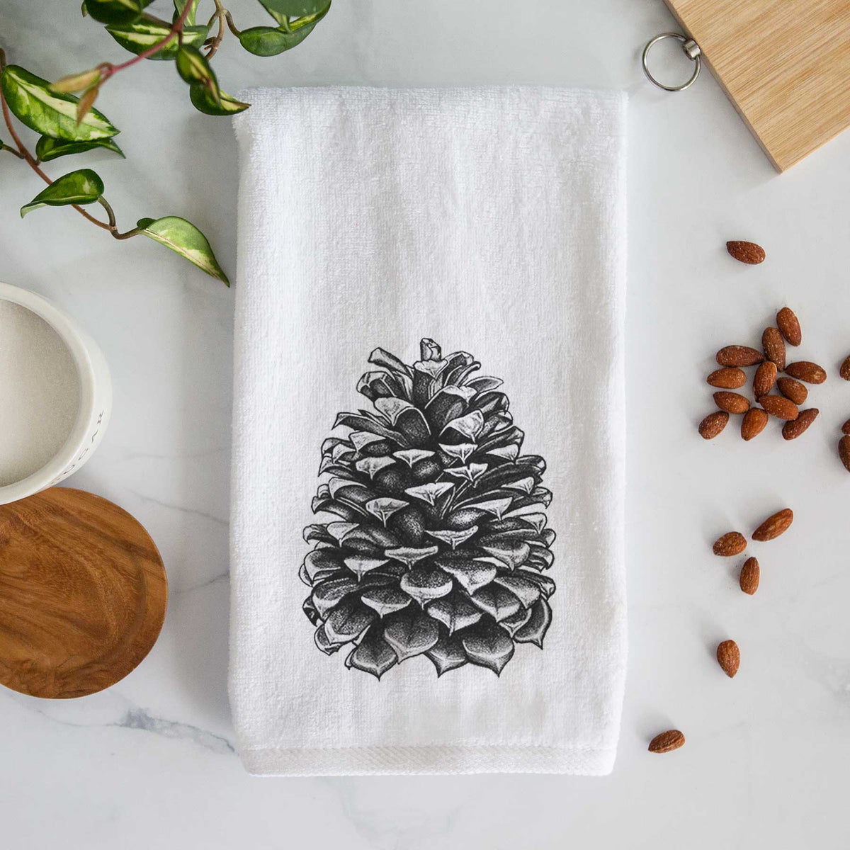 White hand towel printed with a detailed black ink illustration of a large Jeffrey pine cone.