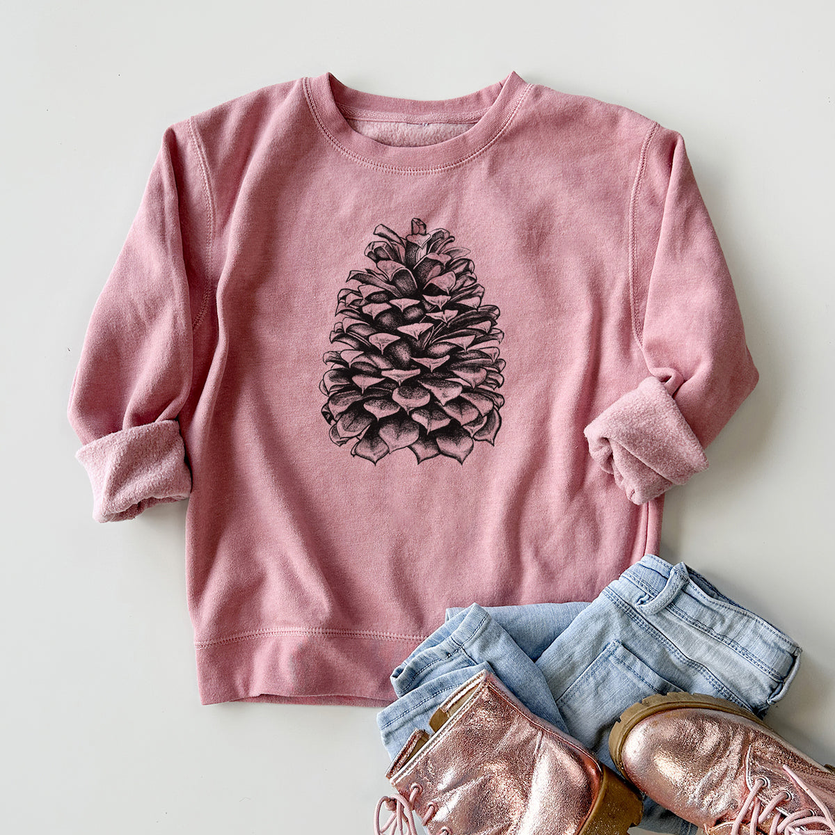 Youth crewneck sweatshirt printed with a detailed black ink illustration of a large Jeffrey pine cone, styled flat with jeans and boots.