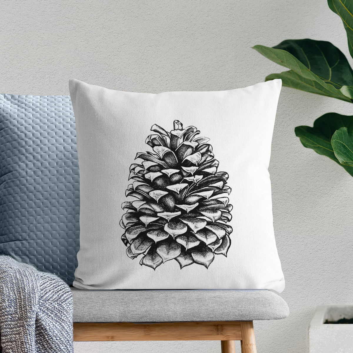 White pillow cover printed with a detailed black ink illustration of a large Jeffrey pine cone, on a bench beside plants.