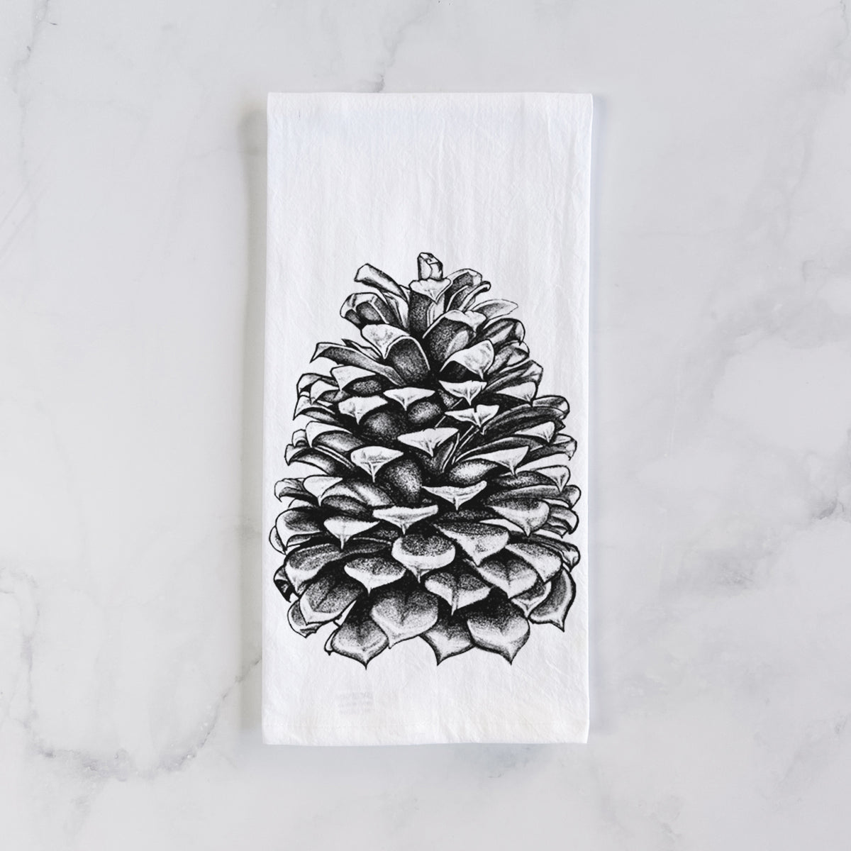 White cotton tea towel laid flat on marble, printed with a detailed black ink illustration of a large Jeffrey pine cone.