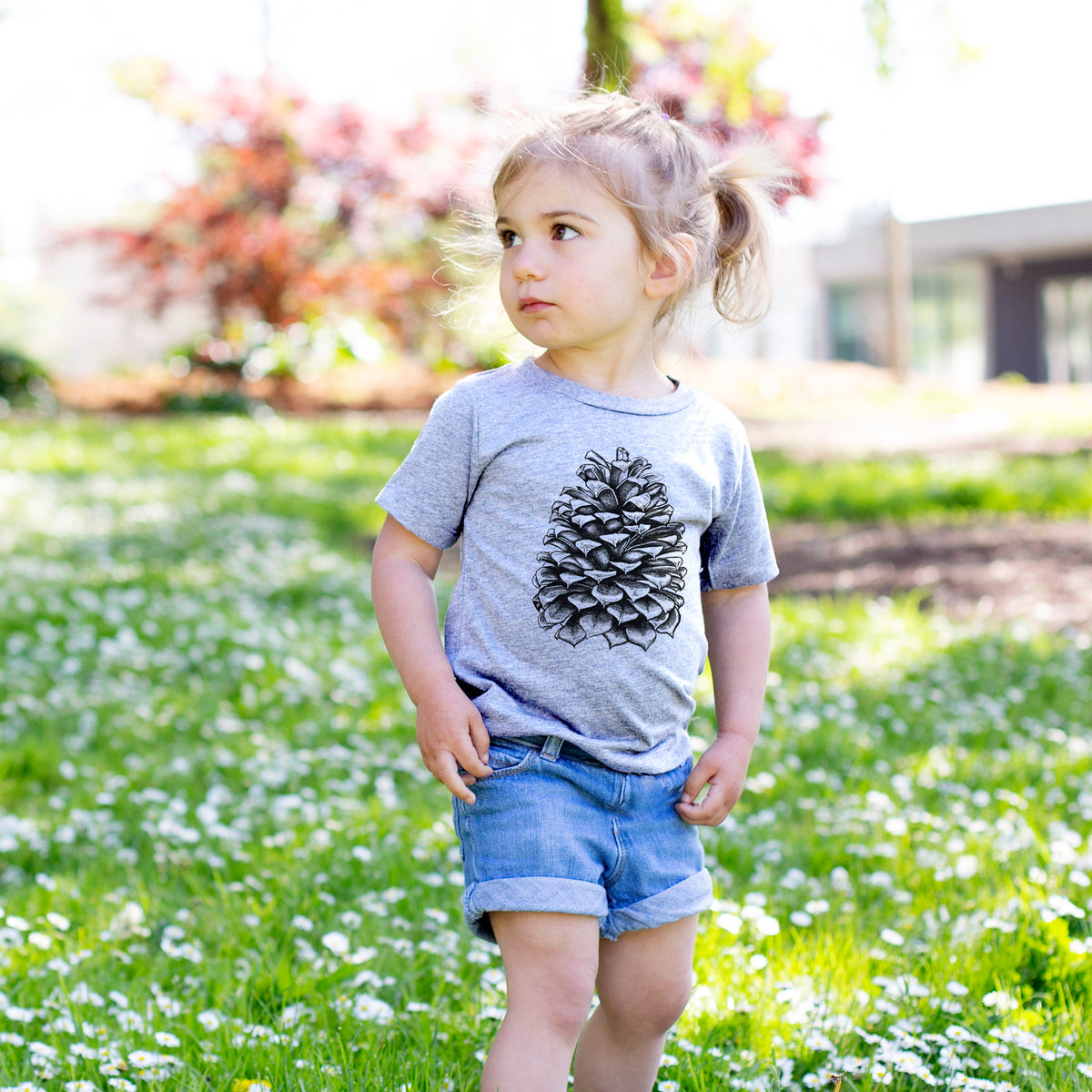 Toddler girl walking outdoors wearing a t-shirt printed with a detailed black ink illustration of a large Jeffrey pine cone.