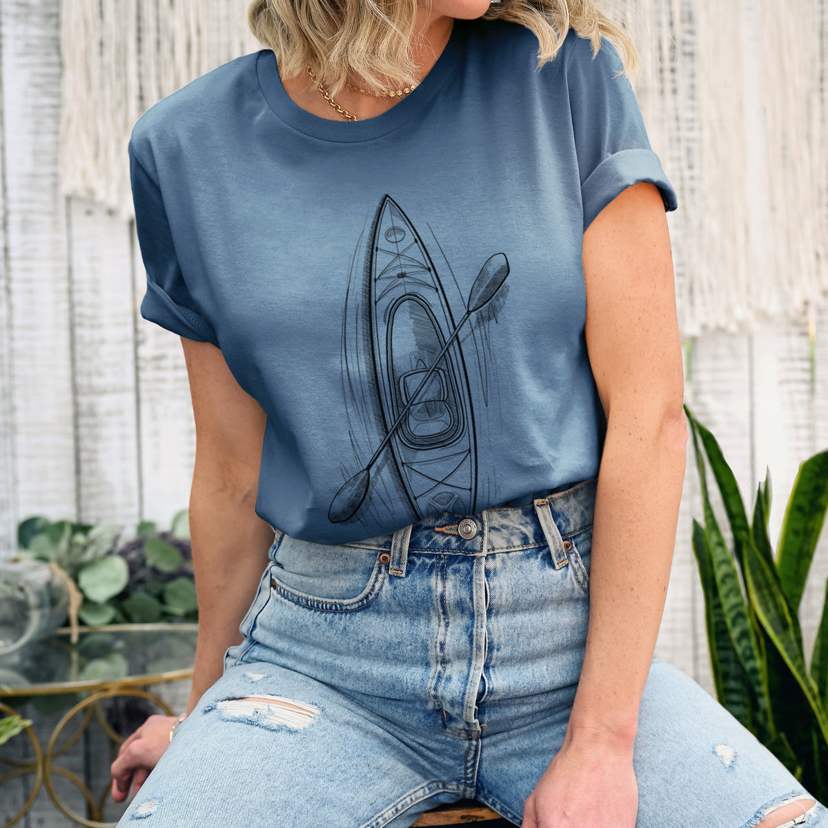 Woman wearing a steel blue lightweight cotton t-shirt printed with a black ink illustration of a kayak with a paddle, seen from above.