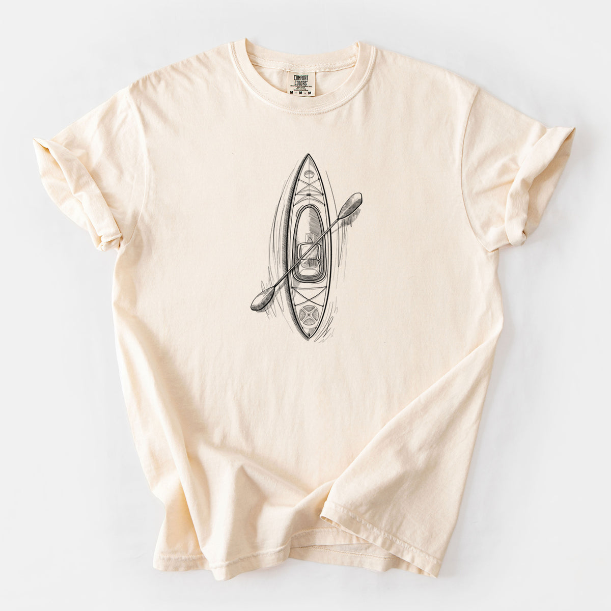 Ivory Comfort Colors t-shirt laid flat, printed with a black ink illustration of a kayak with a paddle, seen from above.