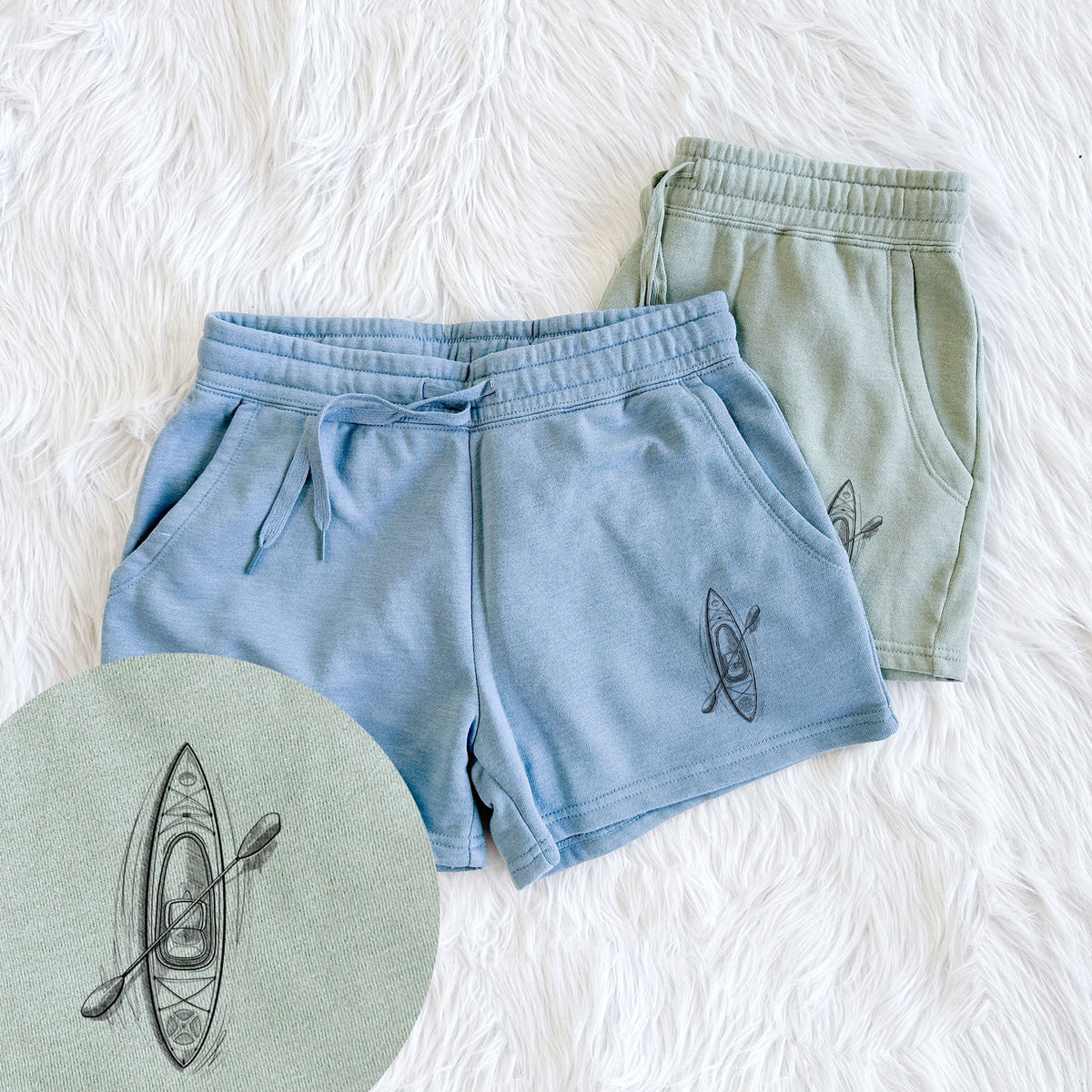 Two pairs of Cali Wave shorts in different colors printed with a black ink illustration of a kayak with a paddle, seen from above, with a close-up of the print.