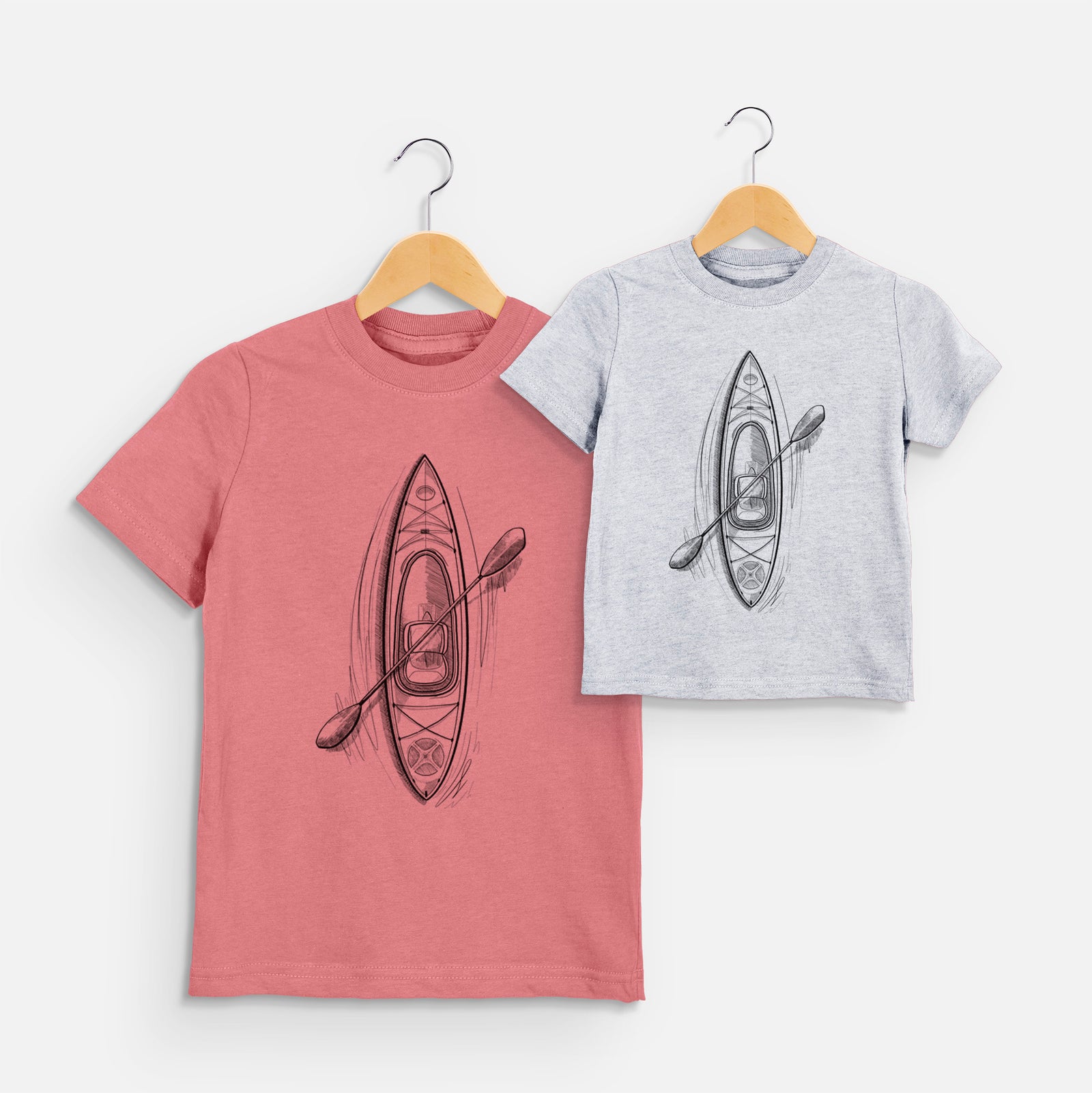Two youth t-shirts in different colors on hangers, printed with a black ink illustration of a kayak with a paddle, seen from above.